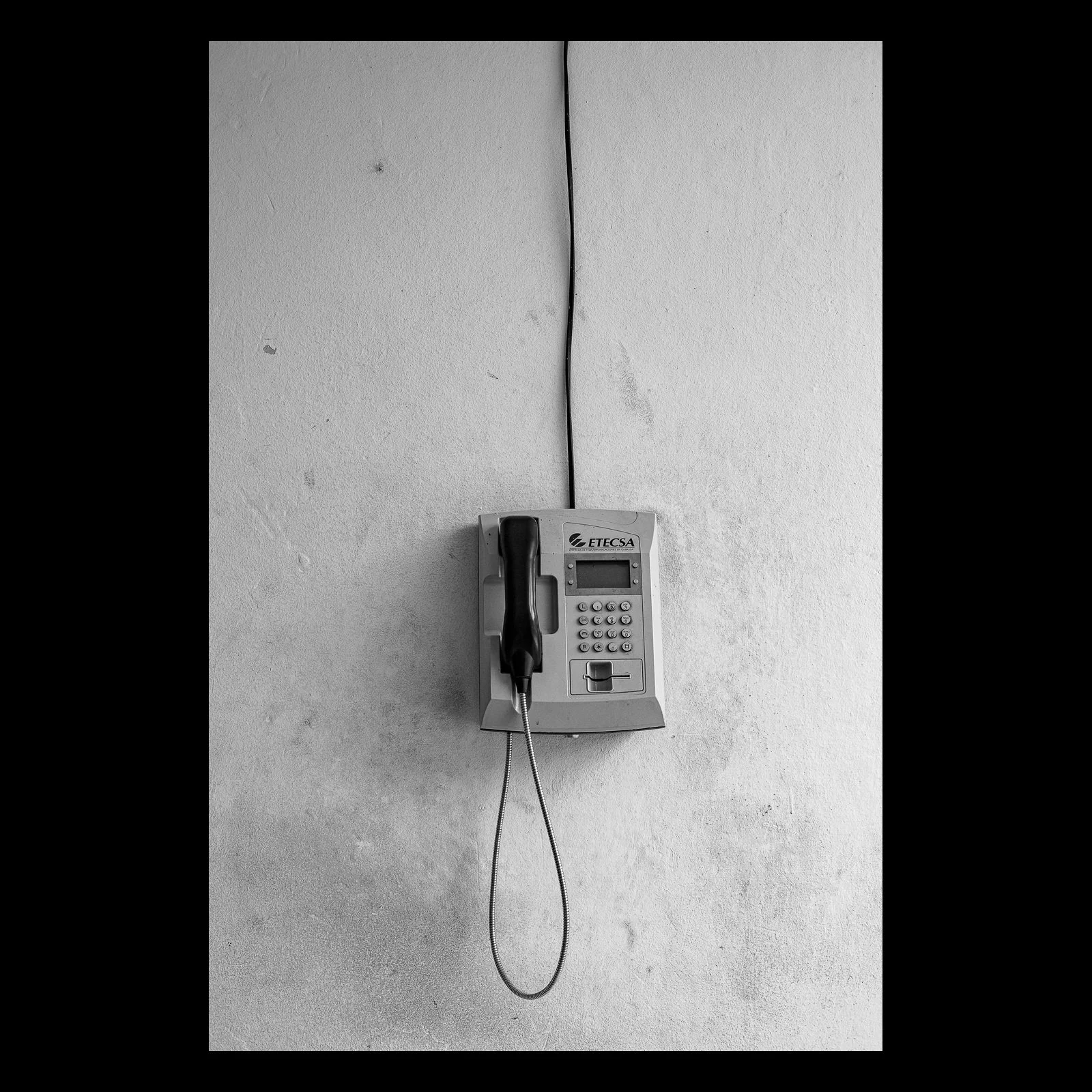 Full-frame black presentation thumbnail of Call Box, showing a simple wall telephone hangs alone on a pale surface in a narrow black-and-white view