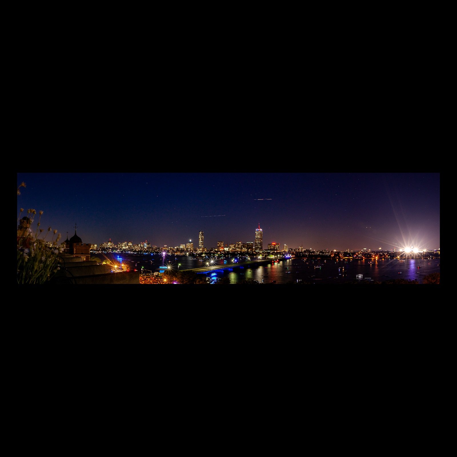 Full-frame black presentation thumbnail of Waterfront After Dark, showing city lights and a bright waterfront flare spread across a narrow nighttime panorama