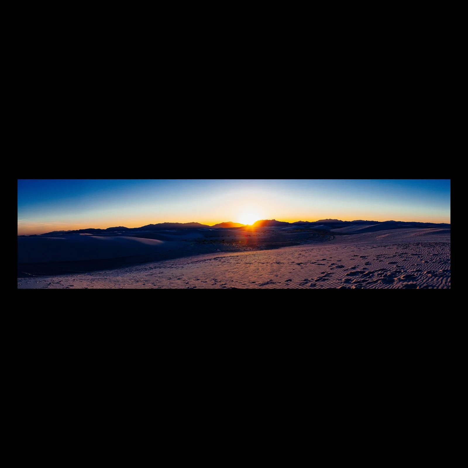 Full-frame black presentation thumbnail of White Sand Dunes, showing the sun touches the horizon beyond rolling snow-covered mountains in a wide panorama