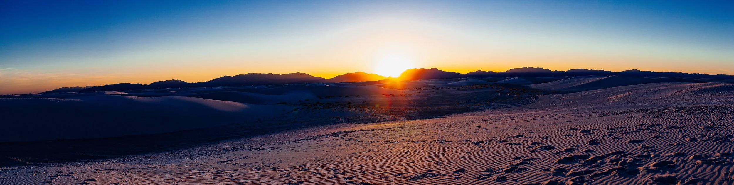 Complete uncropped artwork for White Sand Dunes, showing the sun touches the horizon beyond rolling snow-covered mountains in a wide panorama