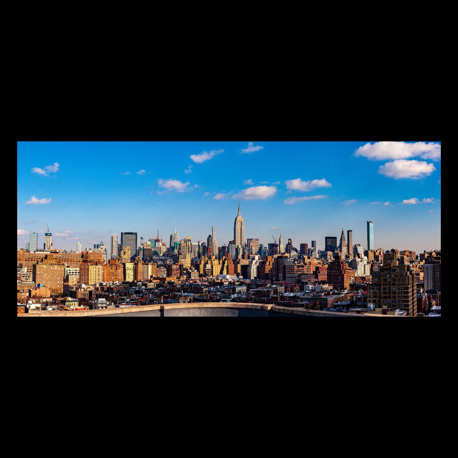 Full-frame black presentation thumbnail of Empire Distance, showing a dense skyline rises beyond brick neighborhoods under a clear blue sky