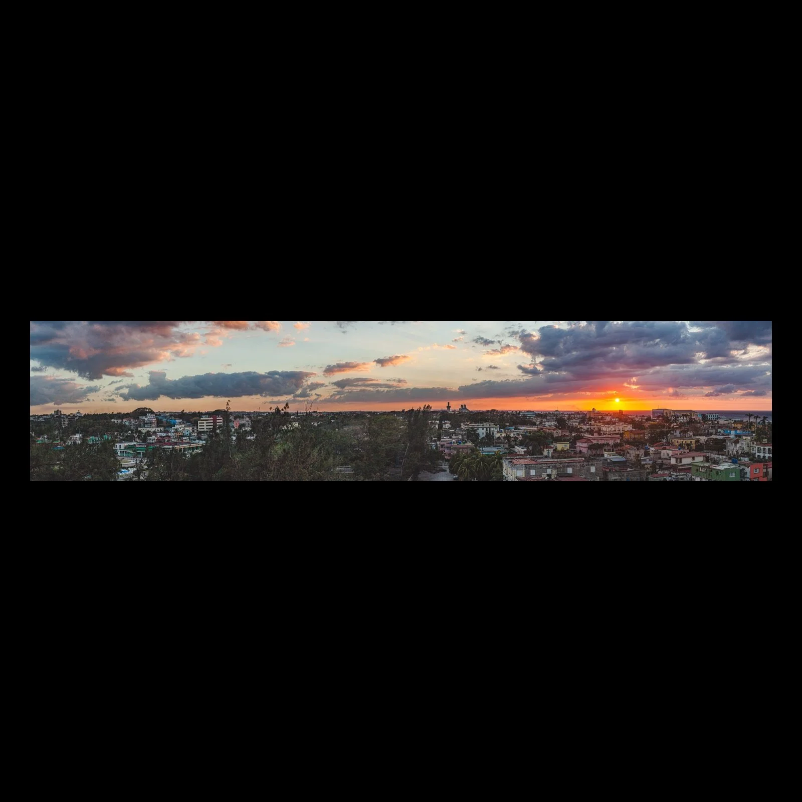 Full-frame black presentation thumbnail of Sunset Over Roofs, showing a red sunset settles behind a broad neighborhood of low roofs and scattered trees