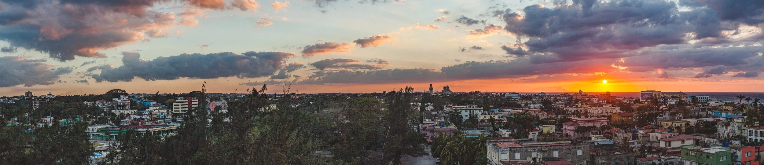 Complete uncropped artwork for Sunset Over Roofs, showing a red sunset settles behind a broad neighborhood of low roofs and scattered trees