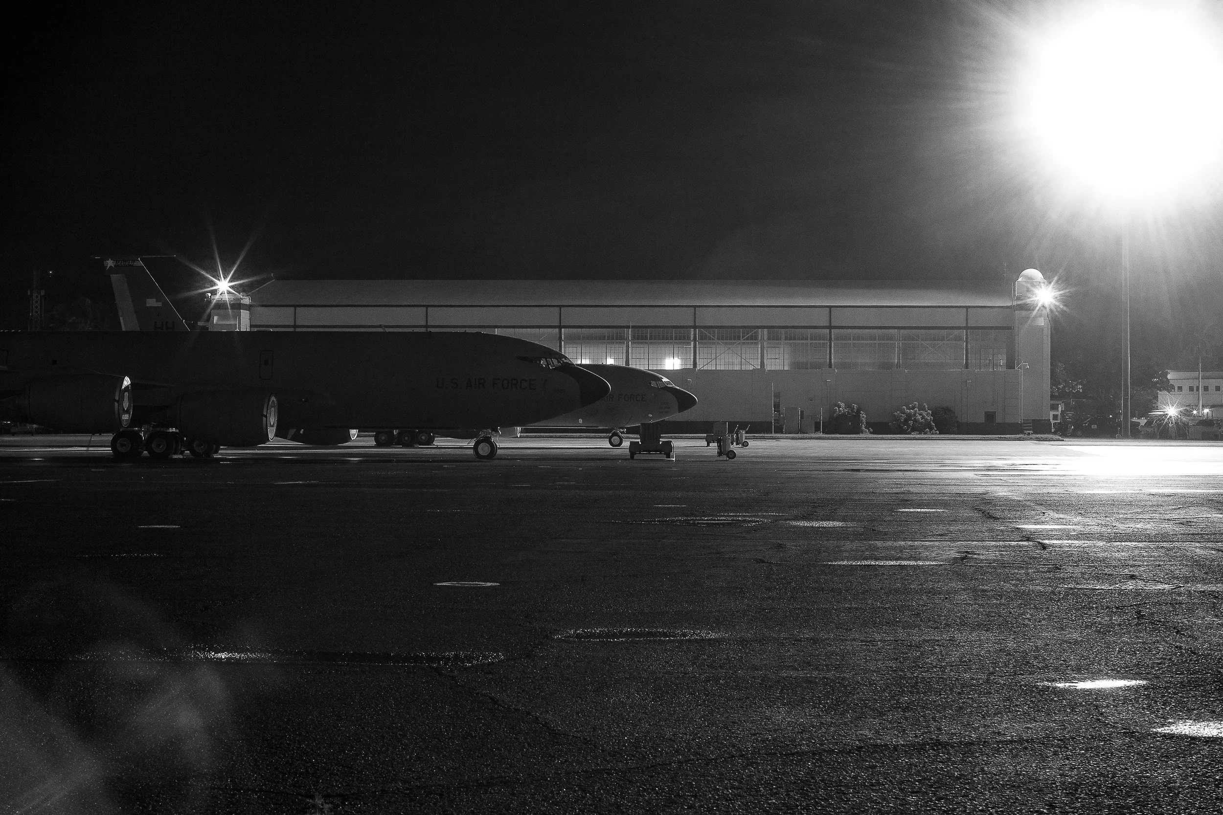 Complete uncropped artwork for Flightline Noir, showing a military aircraft rests beneath intense ramp lights in a grainy black-and-white night scene