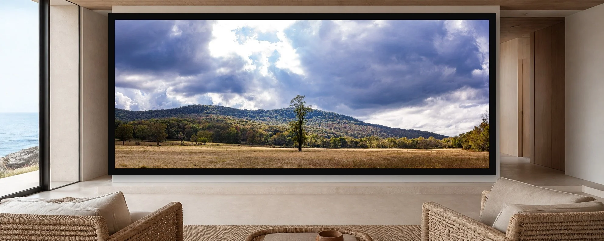 Lone Tree, Moving Weather displayed in a black frame within a restrained coastal residence with pale stone, white oak, woven seating, and a clear central wall