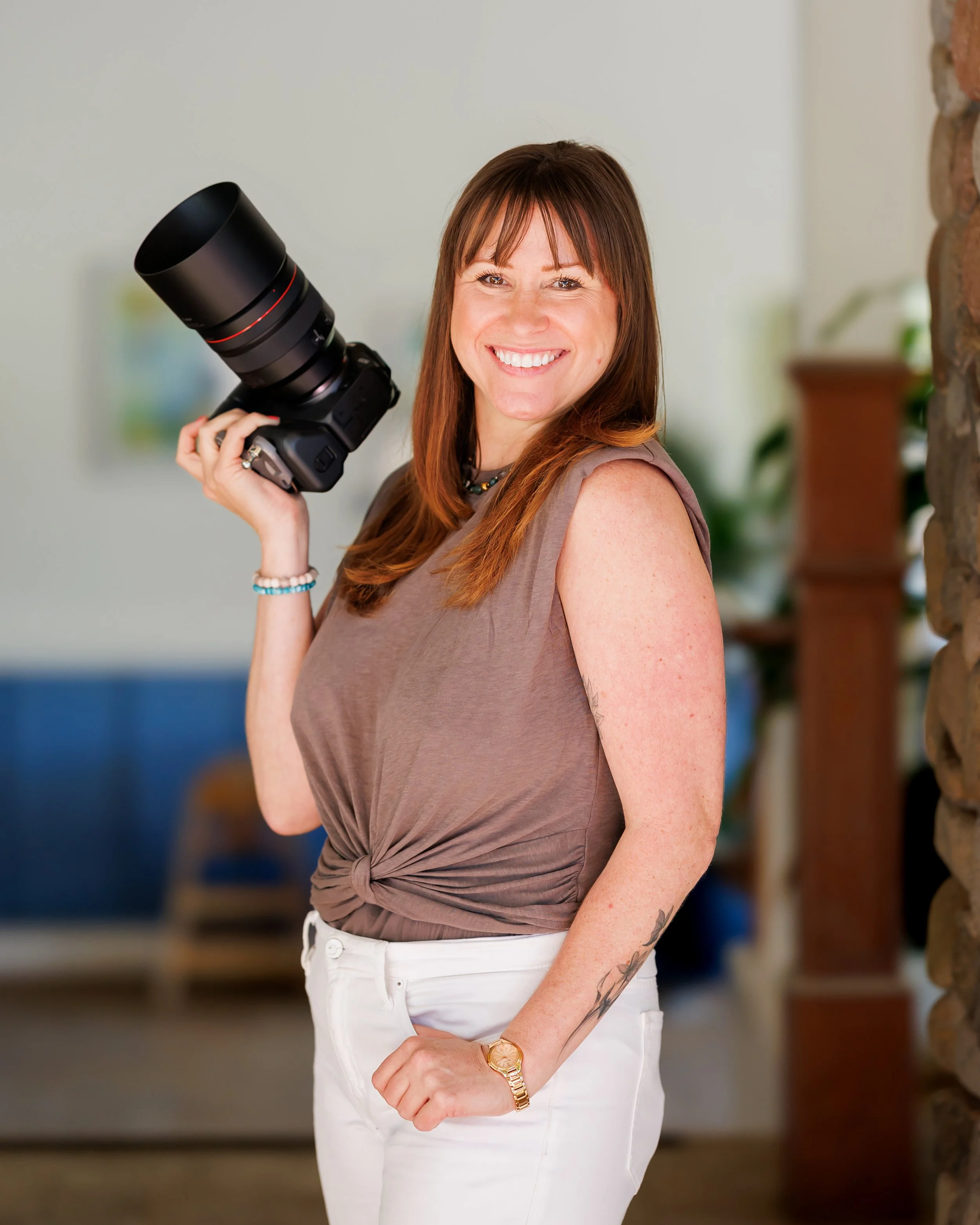 headshot of a woman photographer on maui with brown hair and bangs holding her camera and smiling.