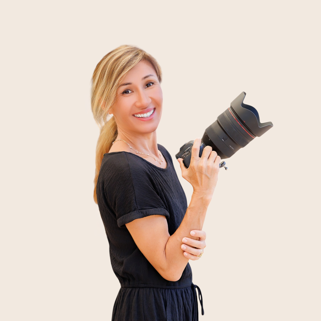 Asain Woman with blonde wavy hair smiling in a black top against a light background.