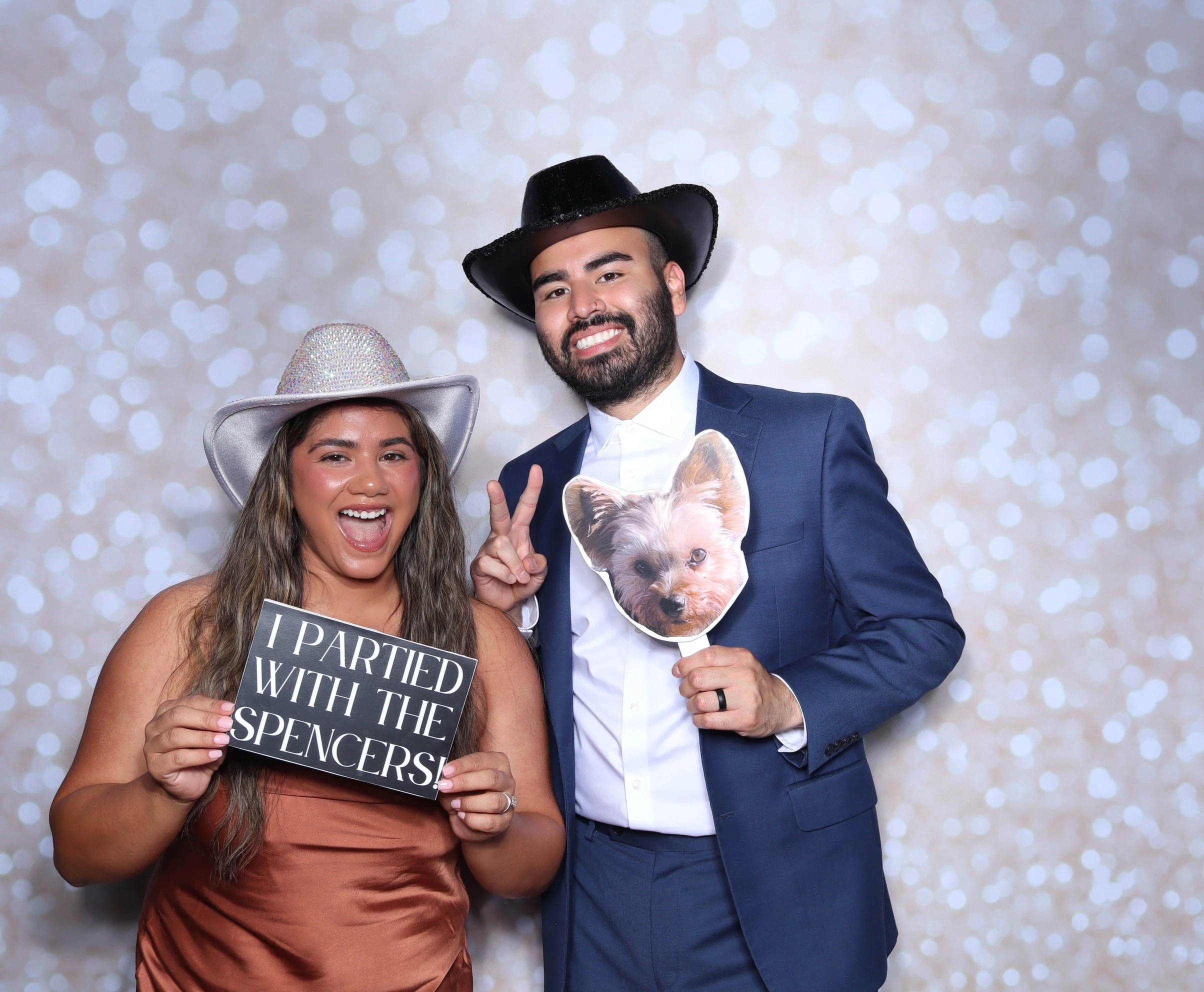 Couple posing with a custom hand held sign and a cut out of a dog with shimmer party hats 