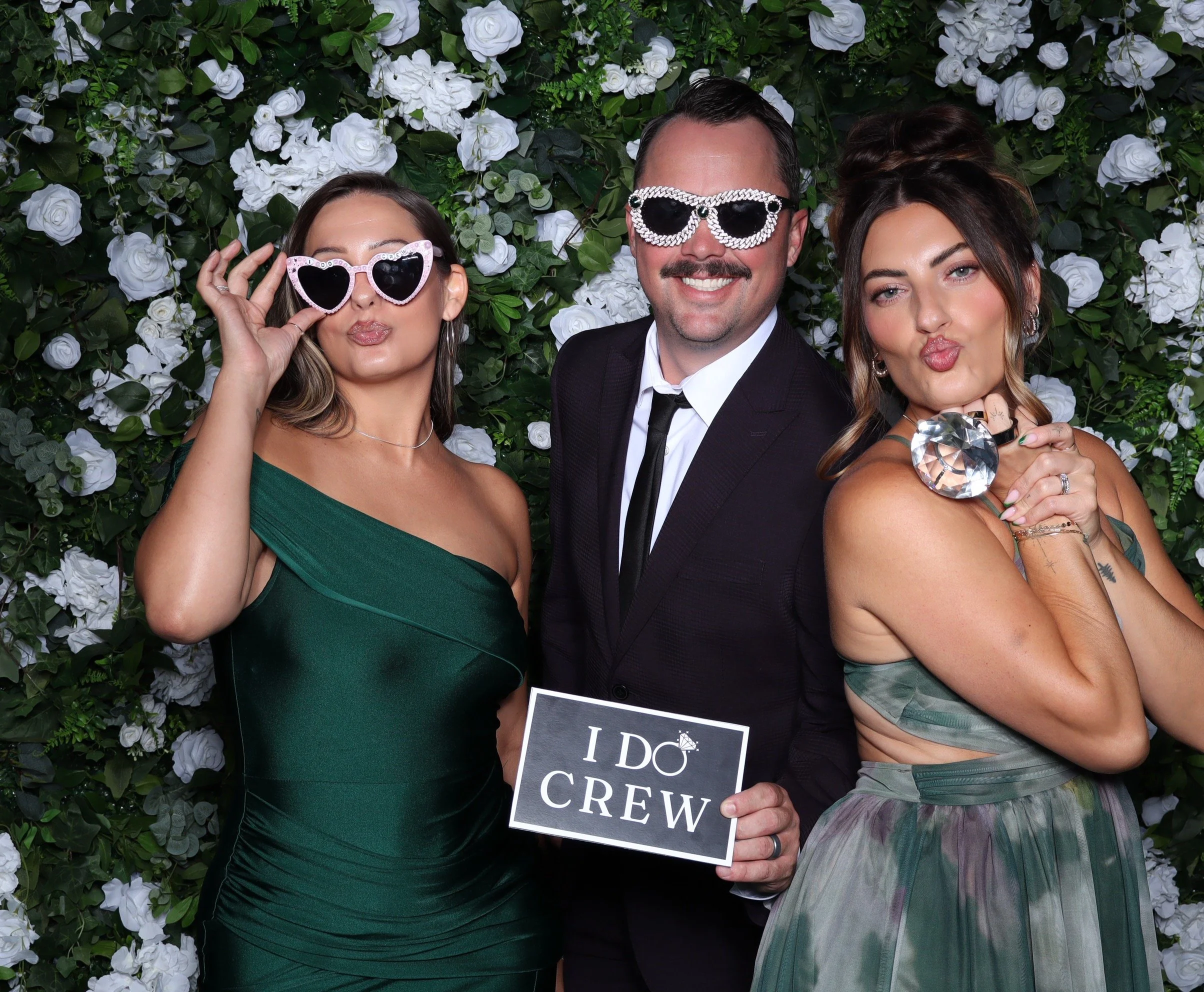 Group of friends posing in front of a flower wall when glasses and " I Do Crew" Sign 