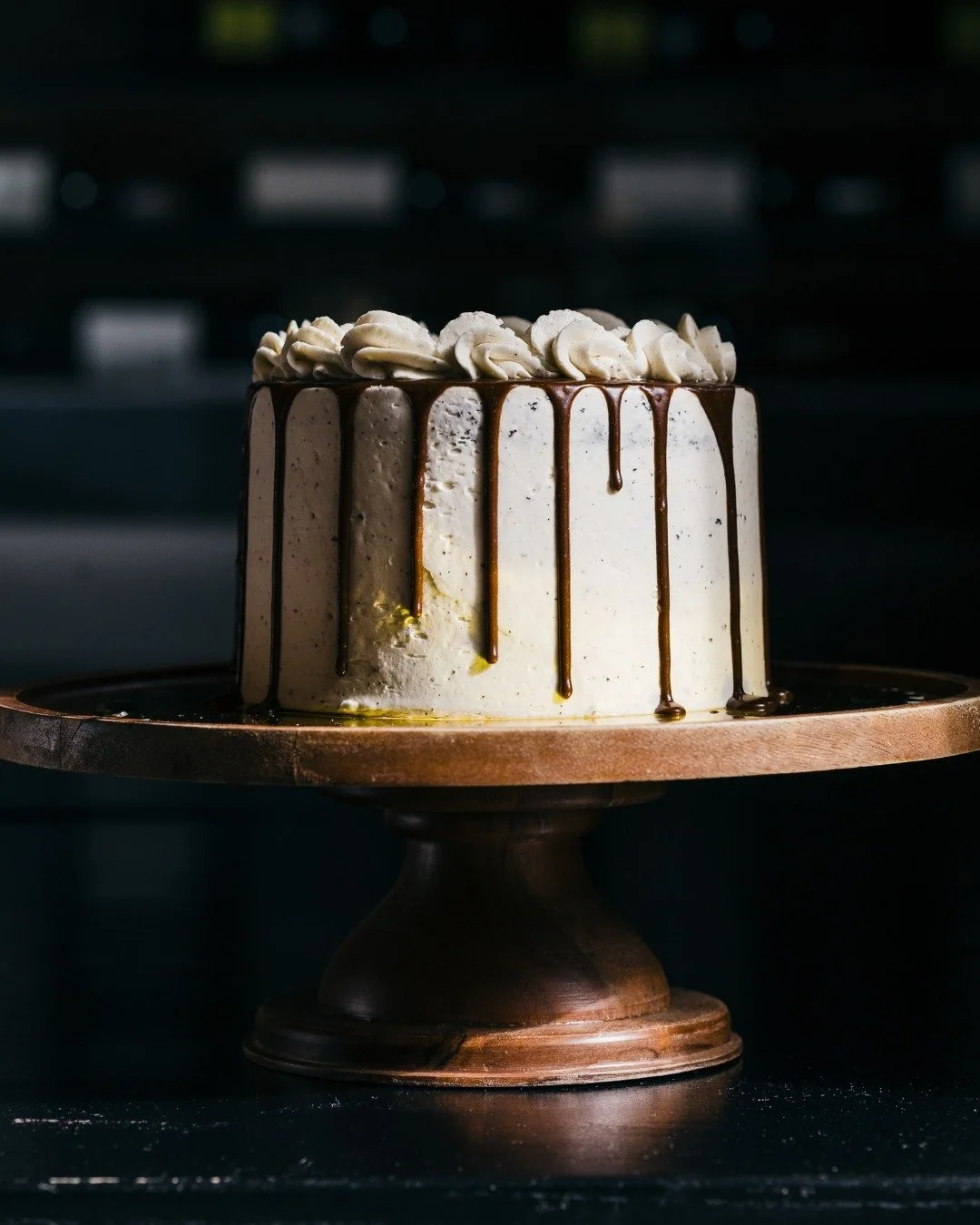 A decorated cake with white frosting and chocolate drips on a wooden cake stand.