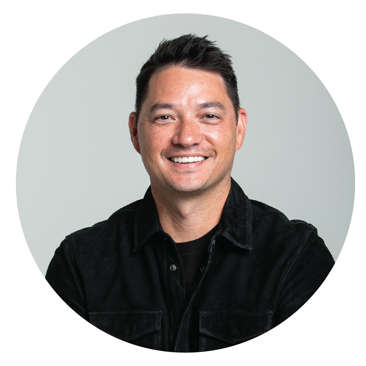 A smiling man with short black hair wearing a black shirt against a light gray background.