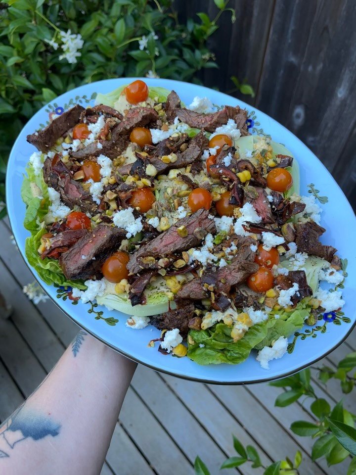 little gem steak salad with creamy pistachio dressing, sungolds, chocolate poblanos, sweet corn, chopped pistachios, za&rsquo;atar, and queso fresco