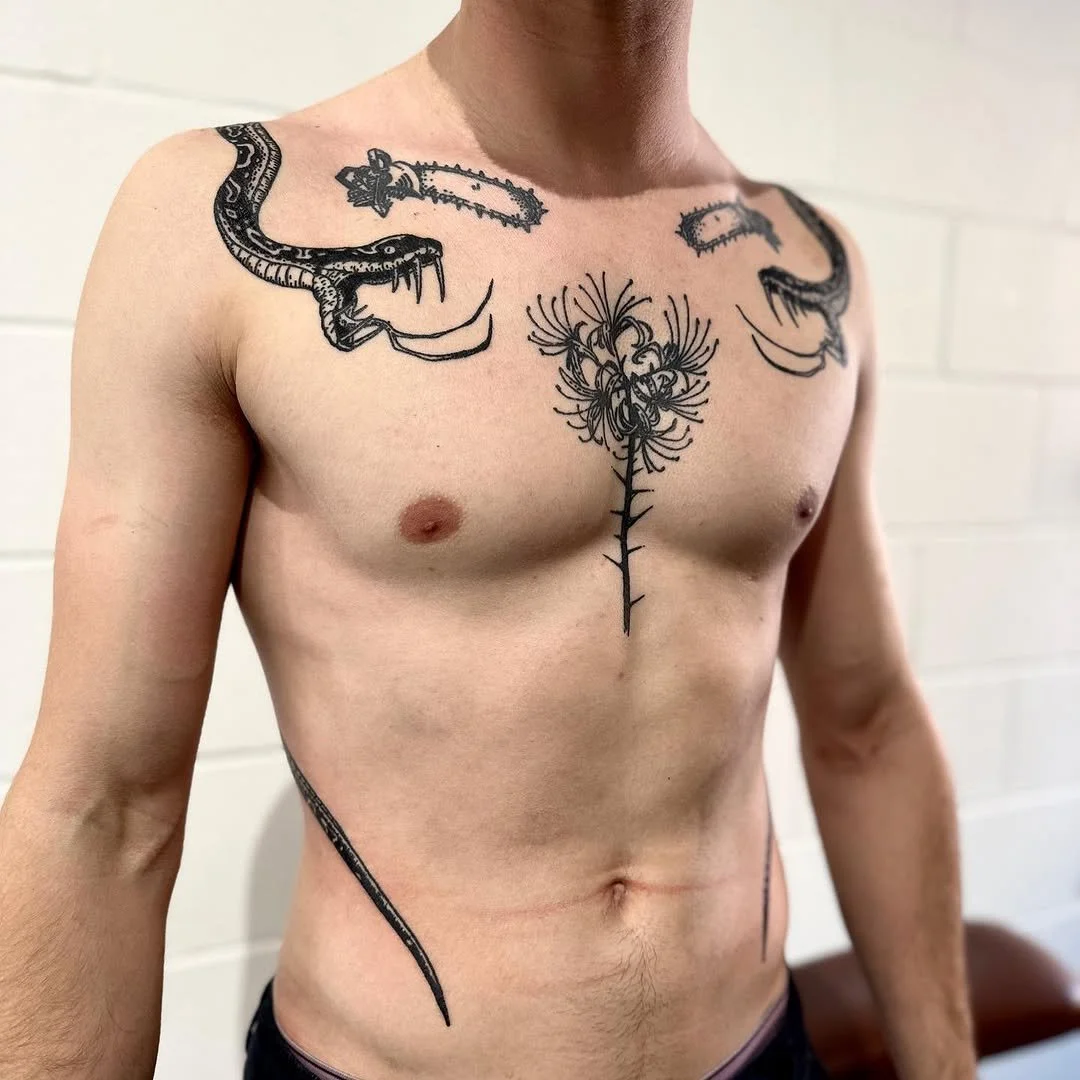 Tattoo of a snake on the left shoulder, a snake on the right shoulder, and a flower tattoo in the centre of the chest.