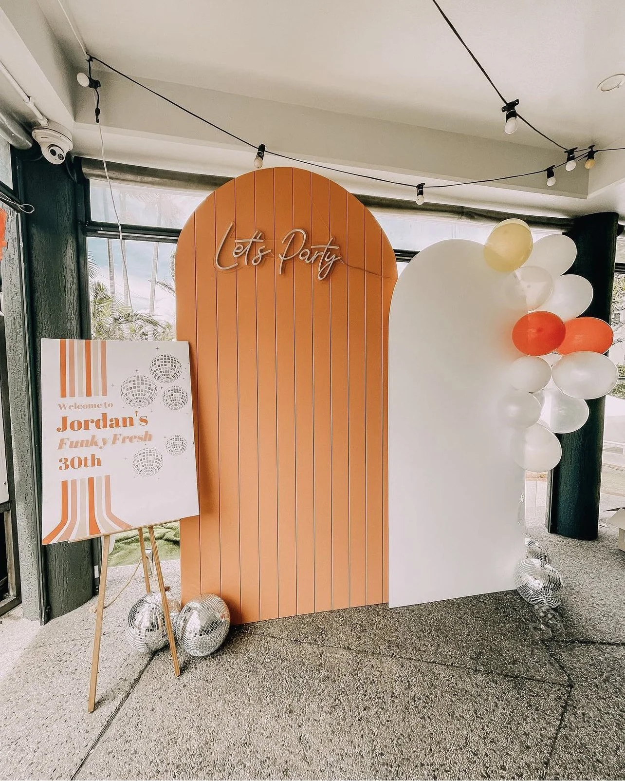 Decorative party backdrop featuring a peach and white color scheme with balloons and a sign welcoming guests to Jordan's 30th birthday celebration.