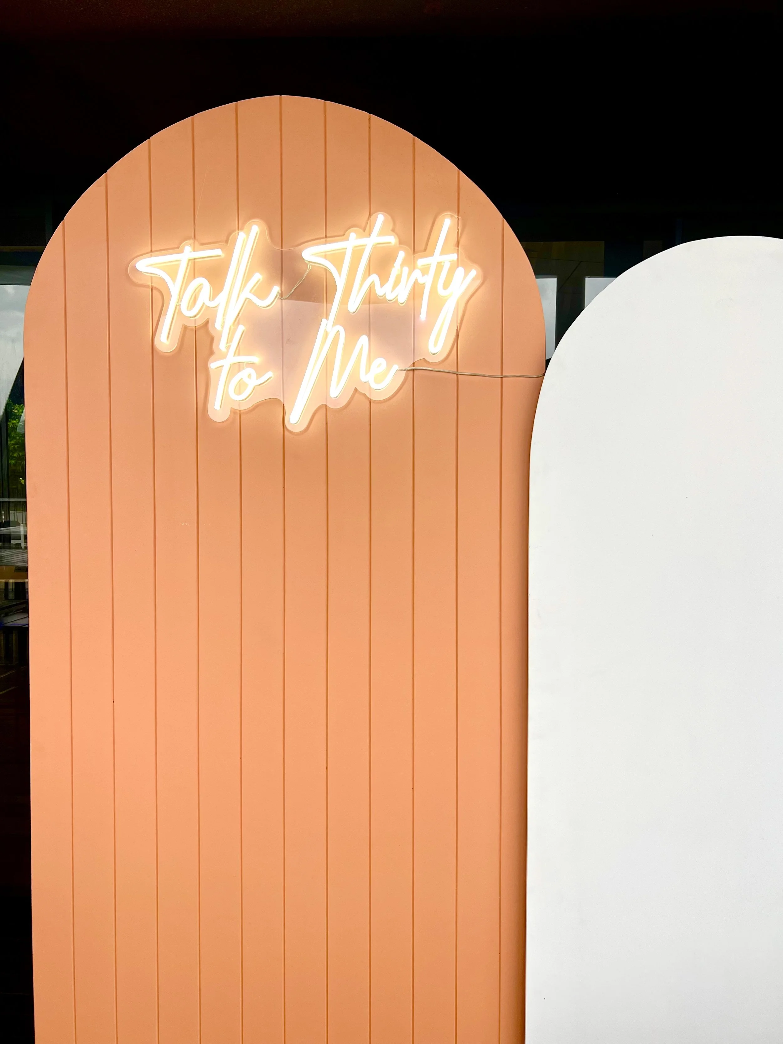 Neon sign reading 'Talk Thirty to Me' on a beige and white background.