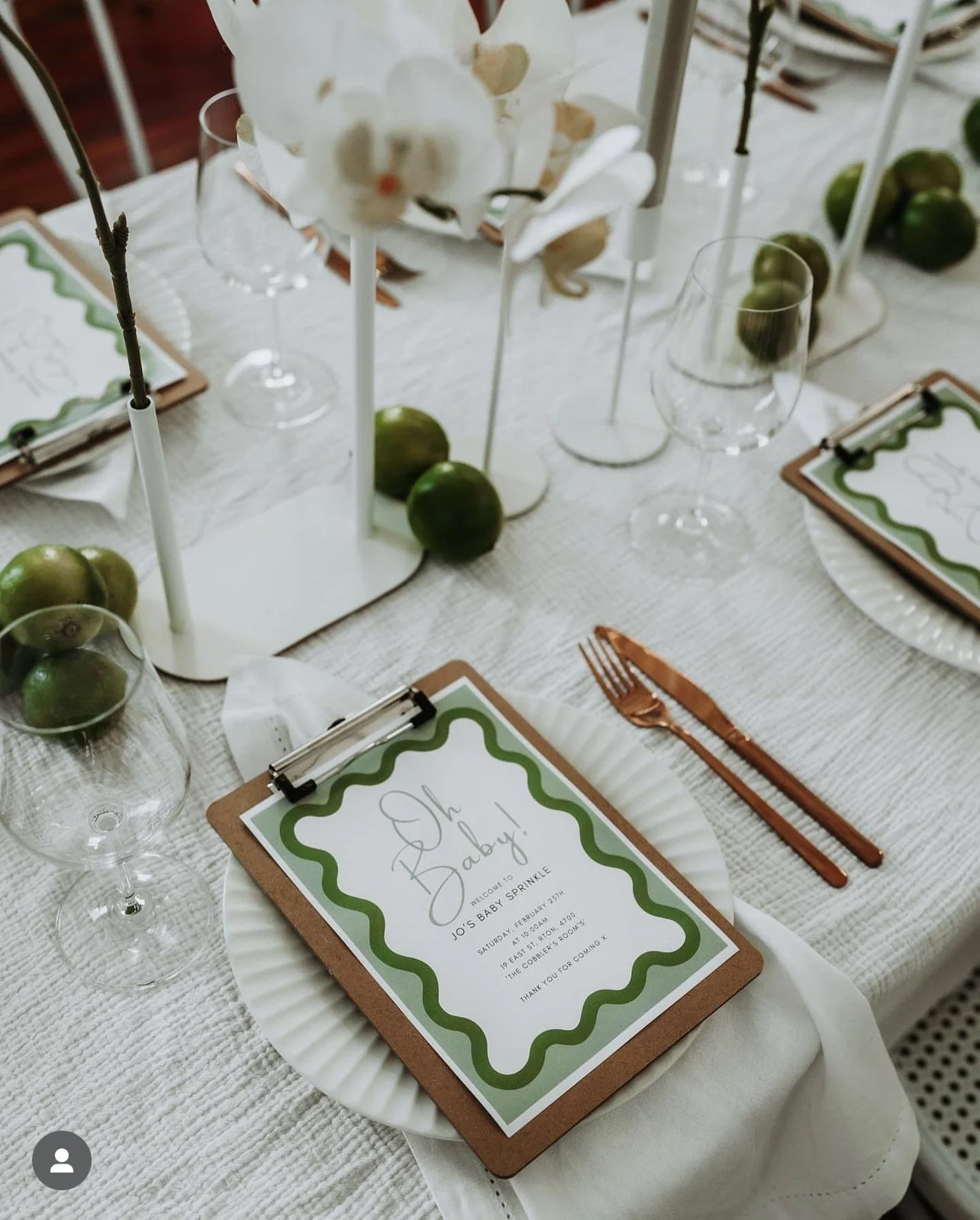 Table set for a baby shower with a sign that reads 'Oh Baby!', green apples, white orchids, and place cards with green borders.