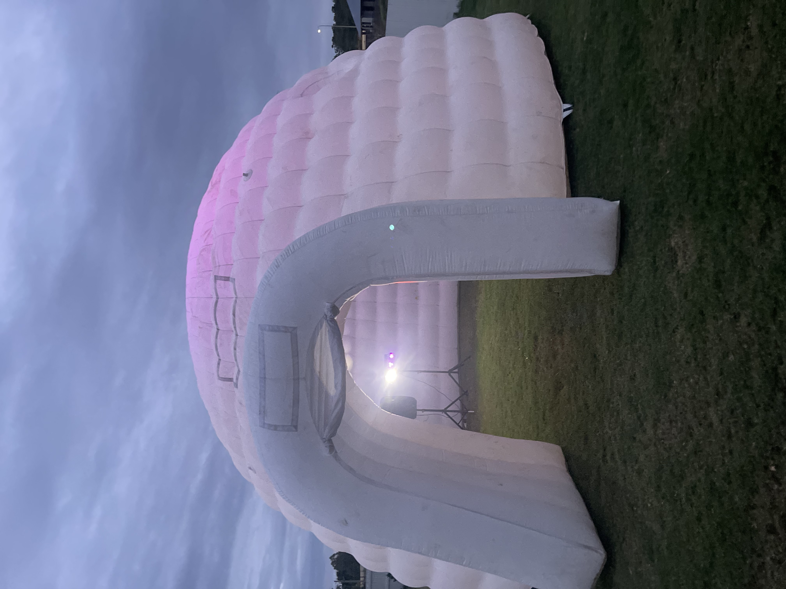 A hot air balloon with a pink and white striped envelope laying on the ground during twilight.