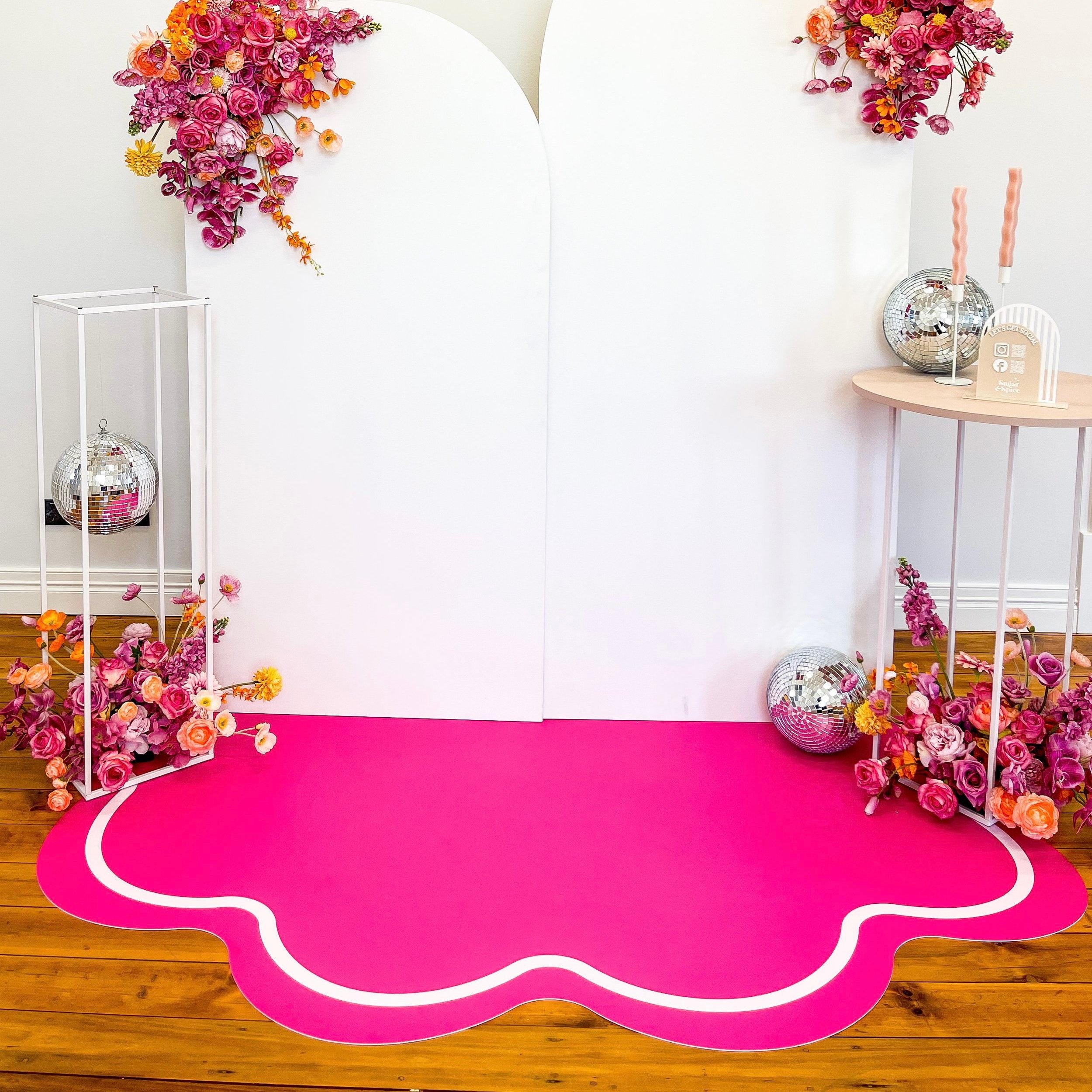 Decorative backdrop with pink and orange flowers, disco balls, pink carpet, and modern furniture for a celebration or photo shoot.