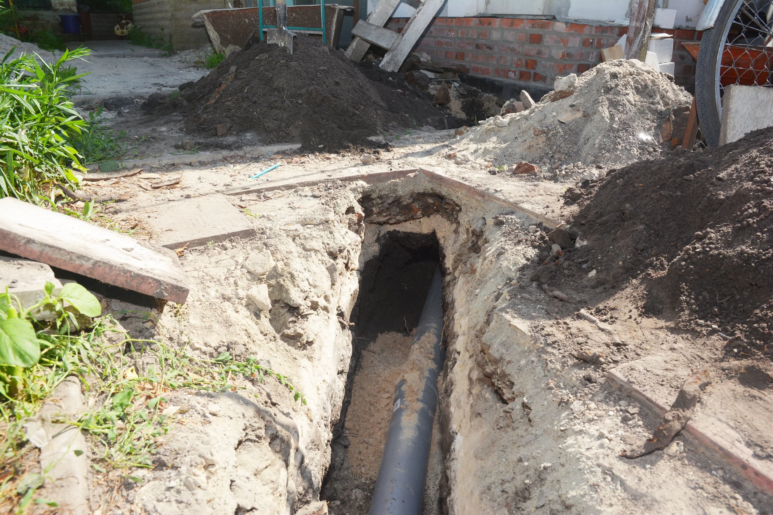 A construction site with a trench and a pipe installed underground, surrounded by dirt and construction materials.