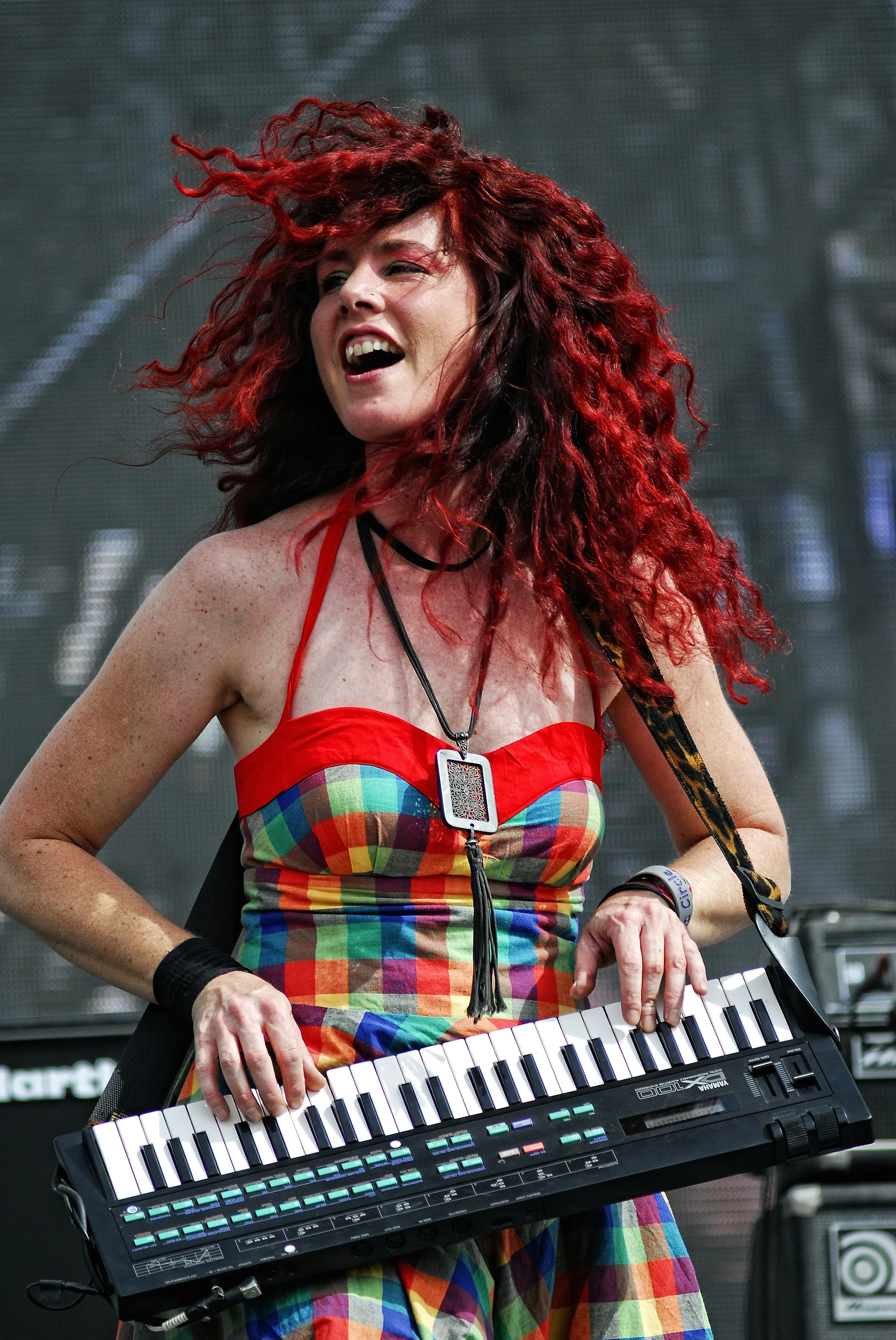 Keyboard player with red hair in colourful check dress sings on stage