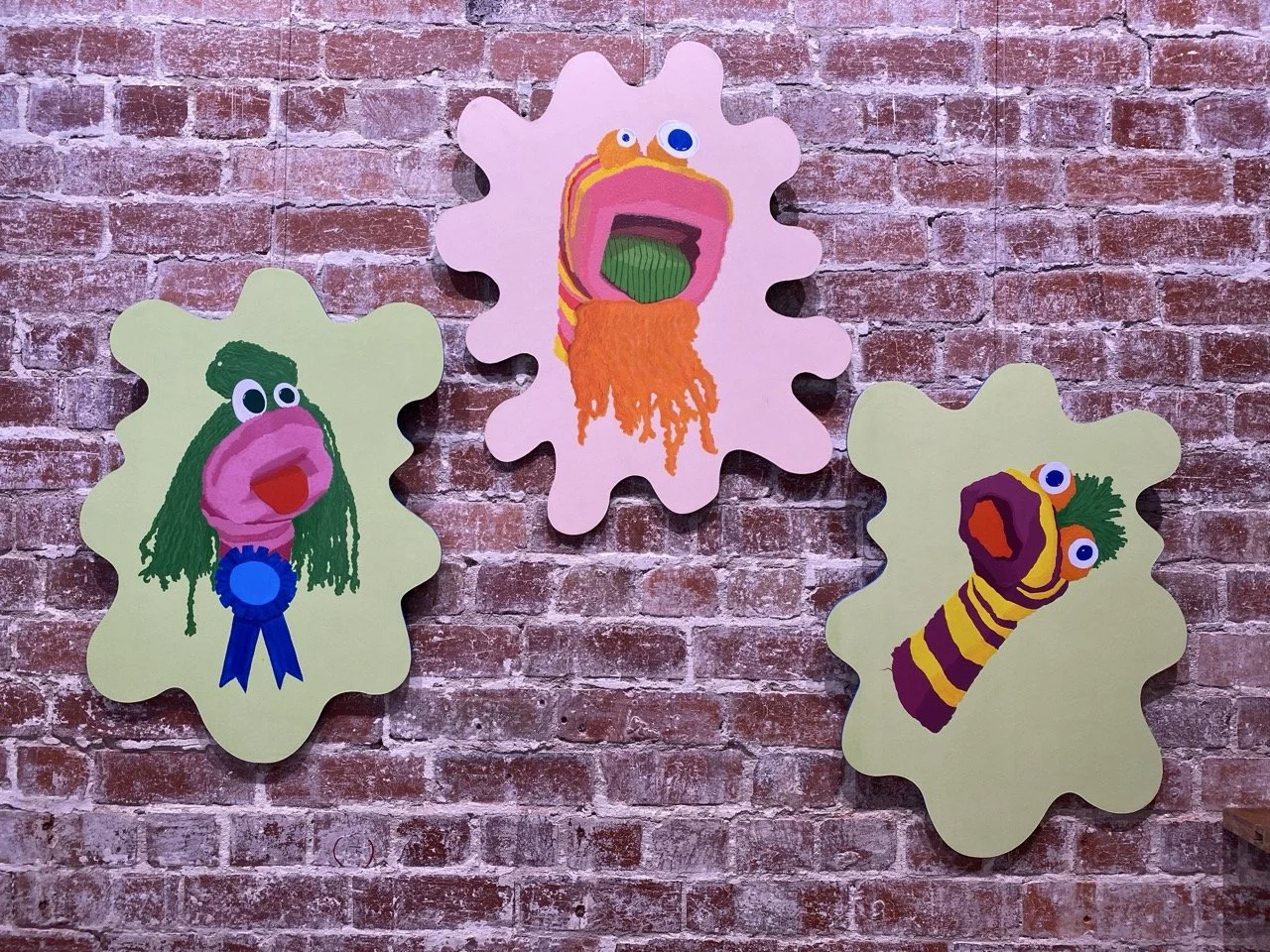 Three painted portraits of sock puppets hanging on a brick wall