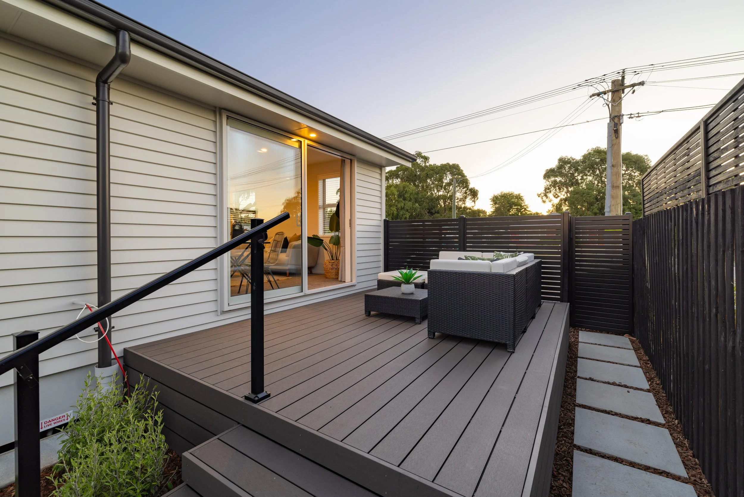 Backyard deck patio with outdoor seating set, potted plants, and a view of trees and power lines at sunset. Sustainable decking products.