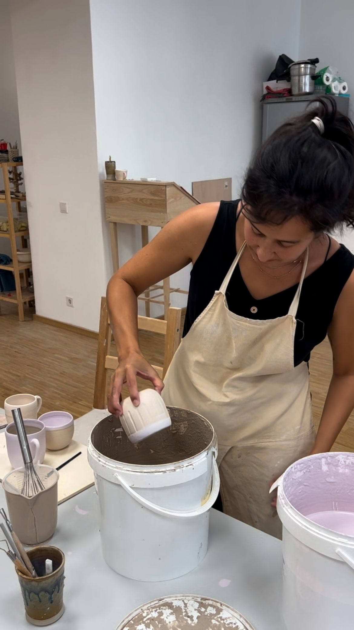 Frau beim Mischen von Keramik- oder Tonmassen in einem großen Behälter in einem Kreativraum.