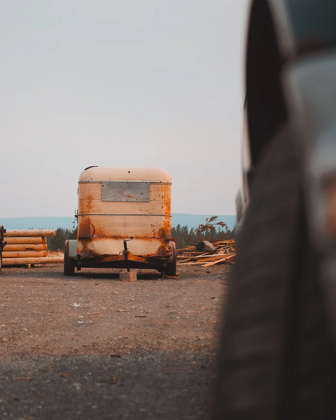 Verroeste, oude aanhangwagen op een stoffige ondergrond, met een bos en bergen op de achtergrond.
