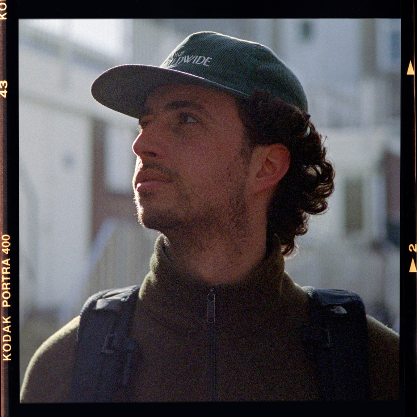 Een jonge man met een pet die naar links kijkt, buiten op een zonnige dag.