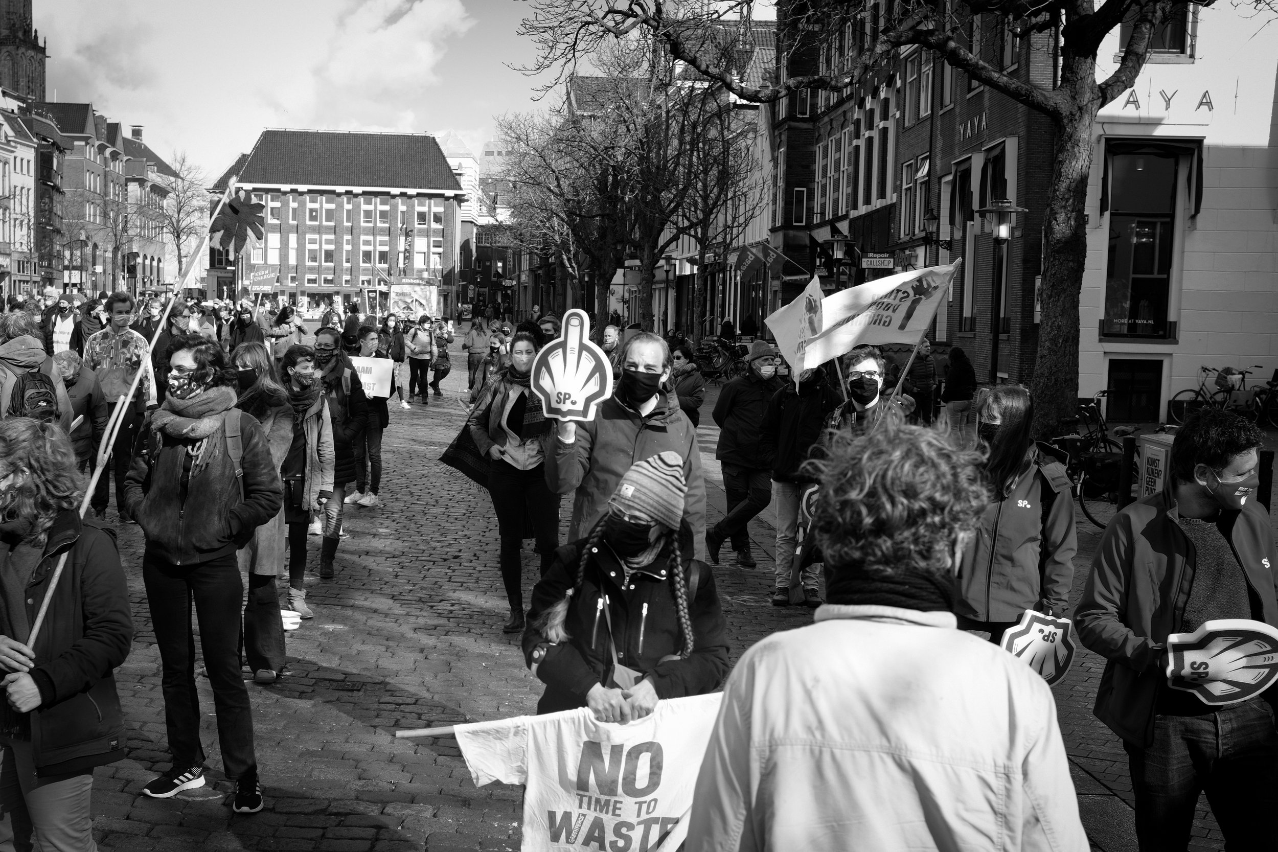Mensen die deelnemen aan een protestmars op straat, sommigen dragen gezichtsmaskers en houden borden en vlaggen vast met anti-waste en klimaatboodschappen.