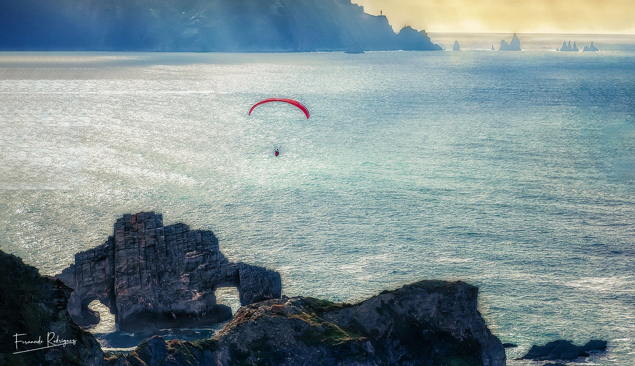 Imagen de un parapente sobrevolando Pena Furada, con el Cabo Ortegal en el horizonte