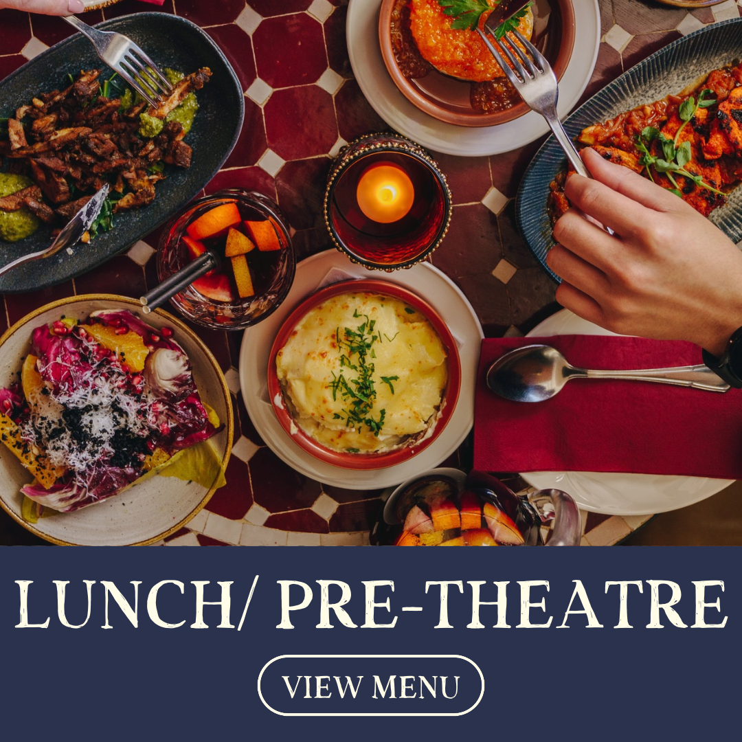 A variety of dishes on a table, including mashed potatoes, pasta with tomato sauce, a salad, and cooked meat, with a lit candle in the center.