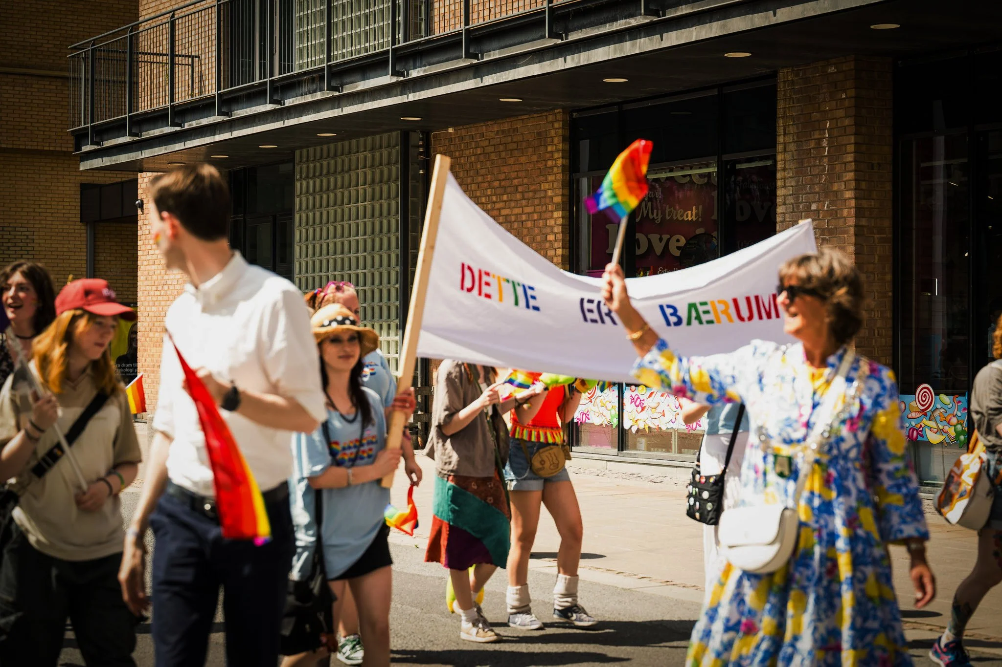 En gruppe mennesker deltar i en parade med regnbuefargede flag og bannere, feirer Pride i byen.