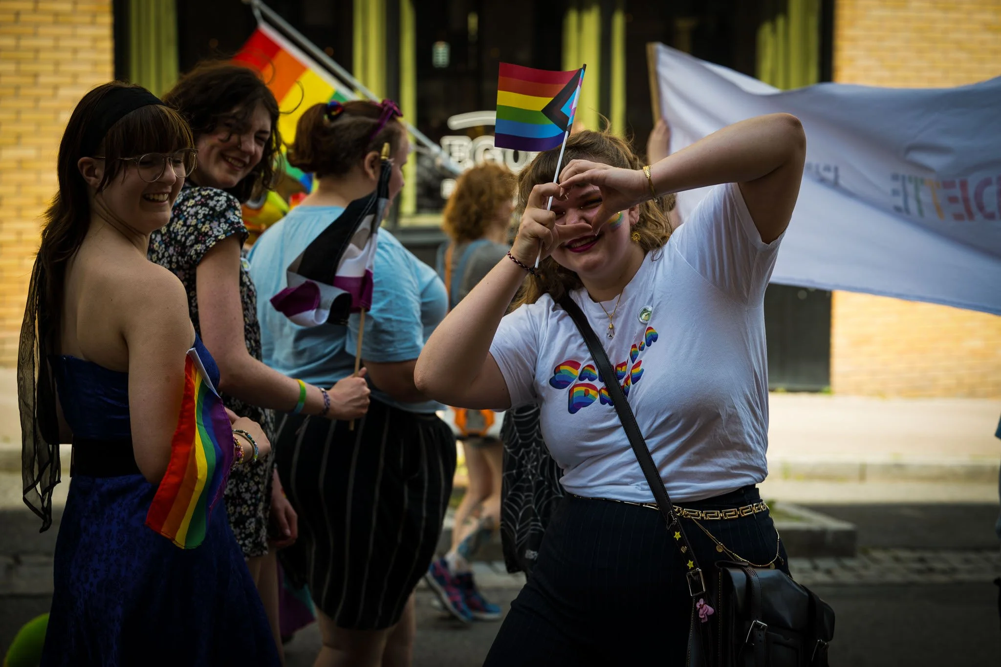 En gruppe mennesker deltar i en parade, mange av dem holder regnbueflagg og har på seg regnbuefargede tilbehør.