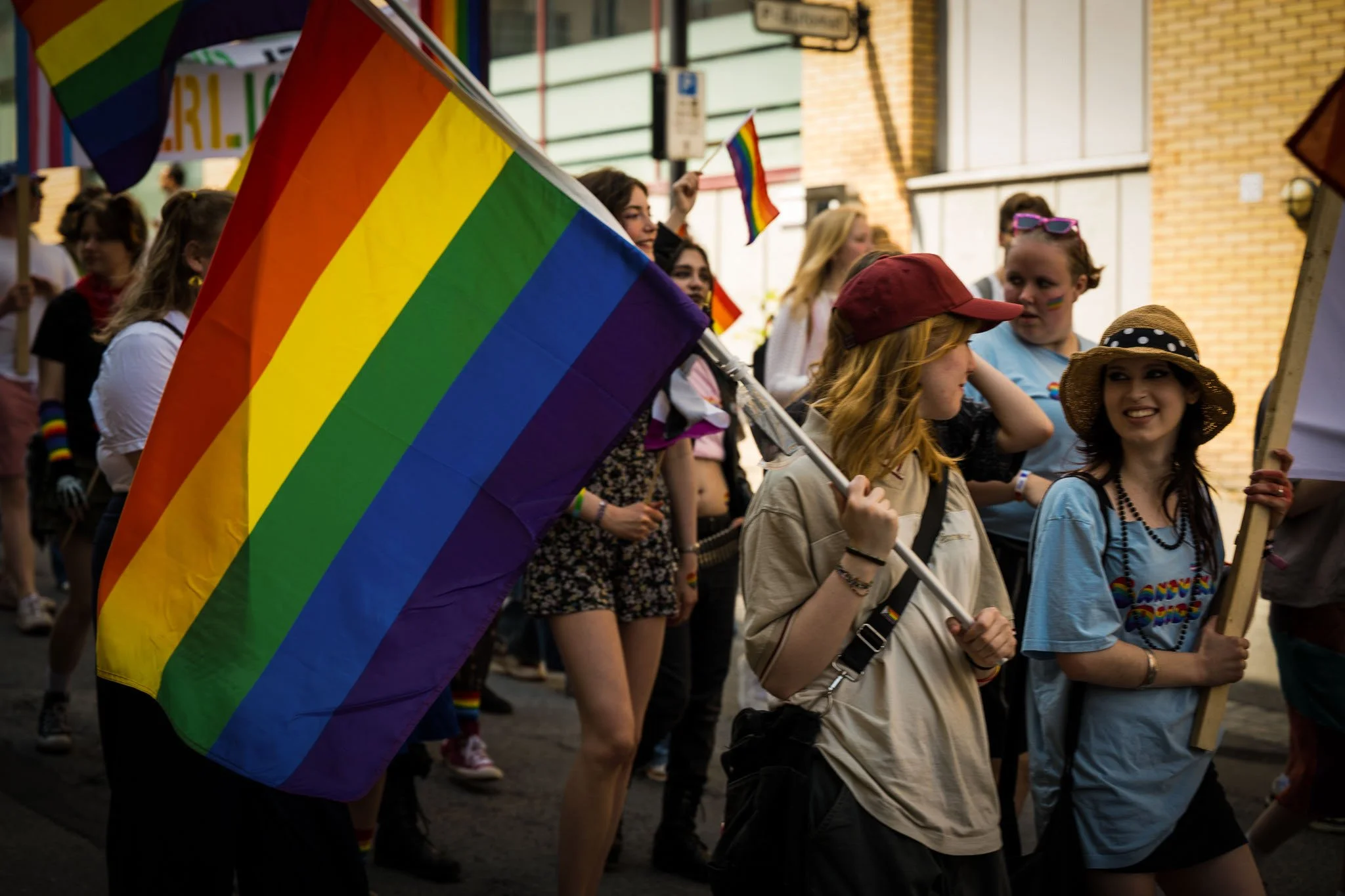 En gruppe mennesker deltar i en Pride-parade, mange holder opp regnbueflagg og har fargerike klær.