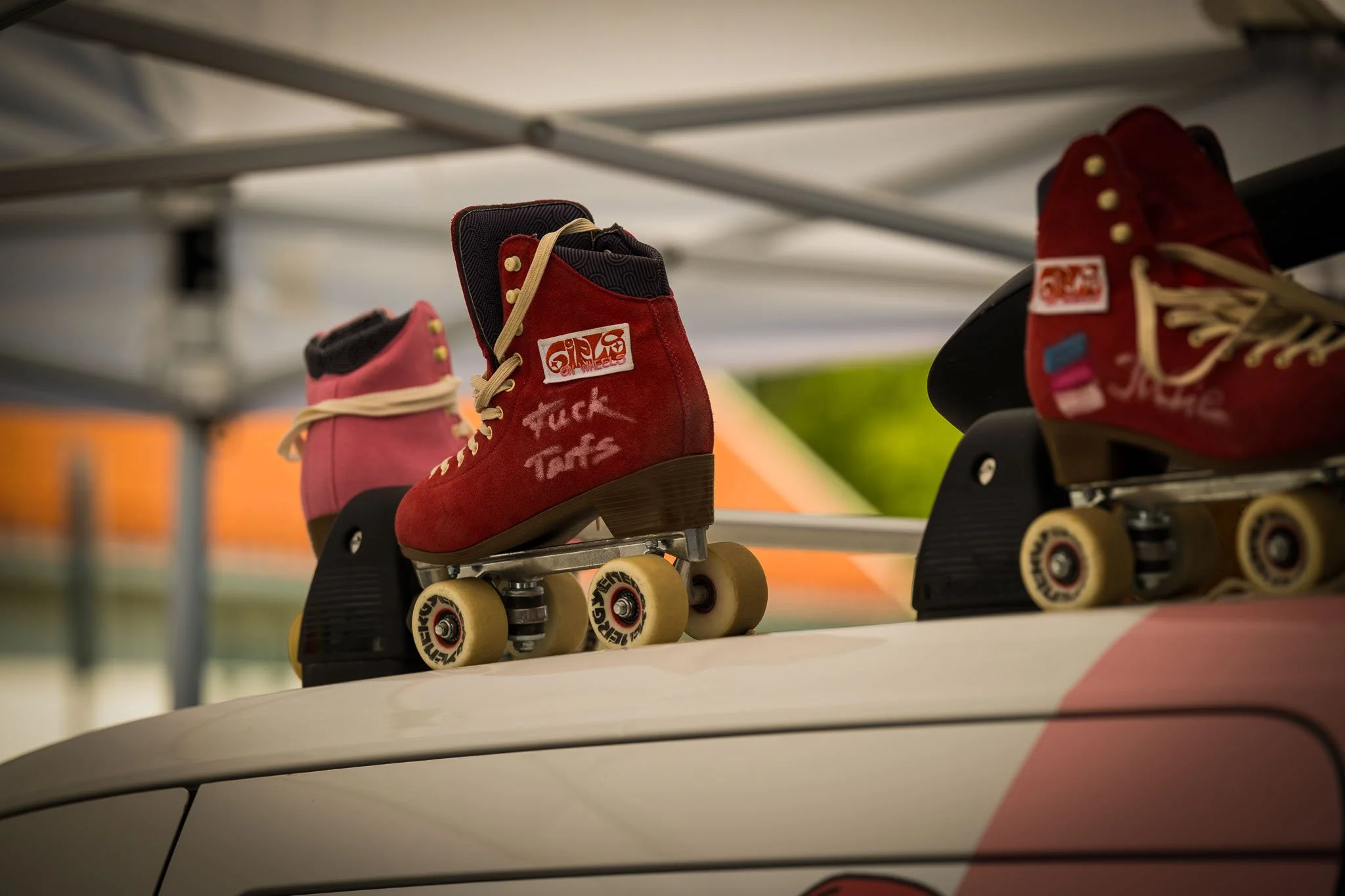 Røde rulleskøyter med beige hjul plassert på taket av en hvit bil under en blå og hvit markise.