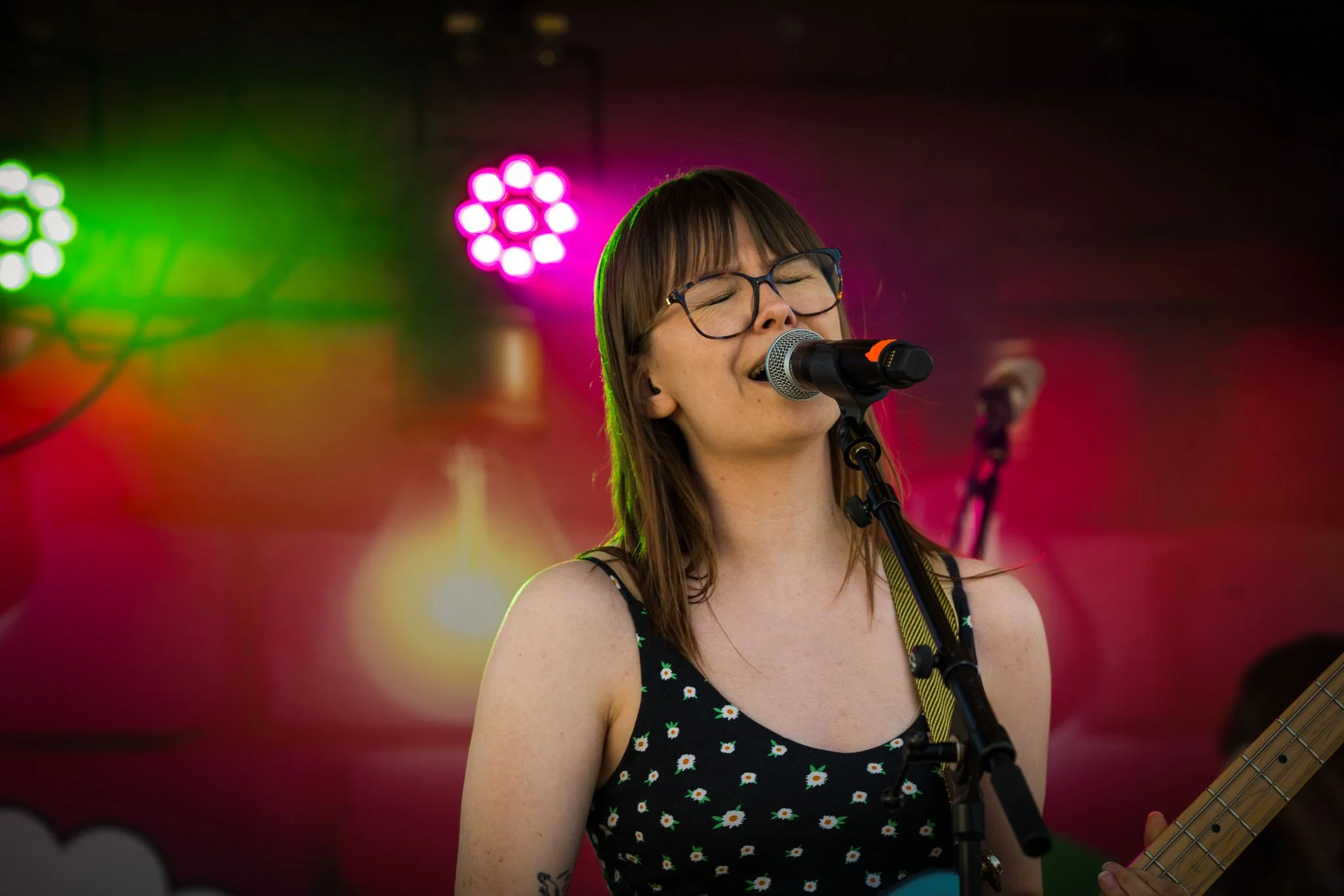 En kvinne med briller synger og spiller gitar på scenen, omgitt av fargerike lys.