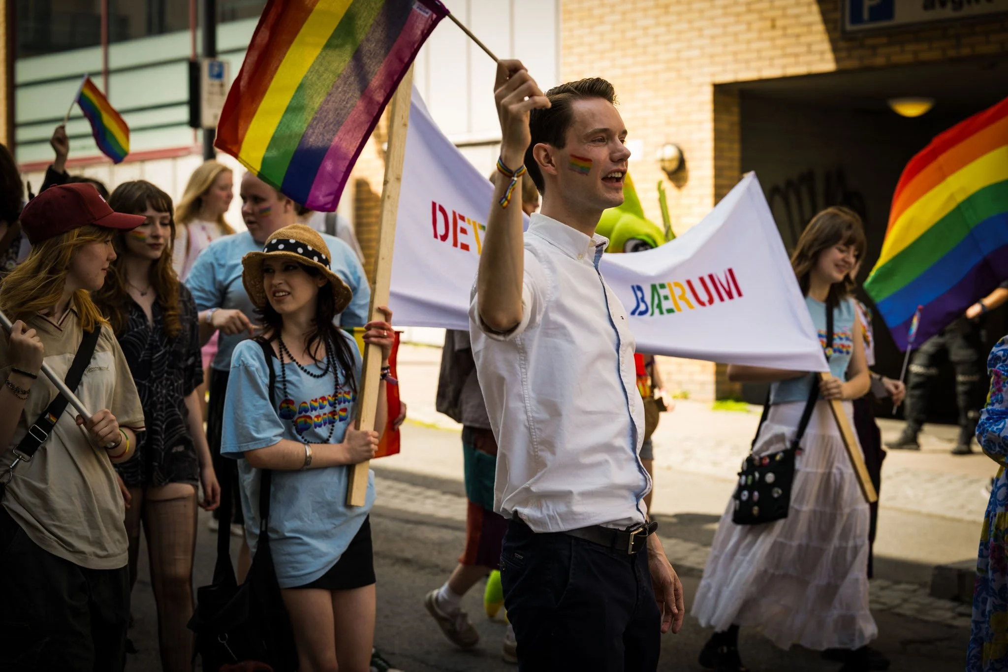 En gruppe mennesker deltar i en parade med regnbueflagg og bunad i Norge.