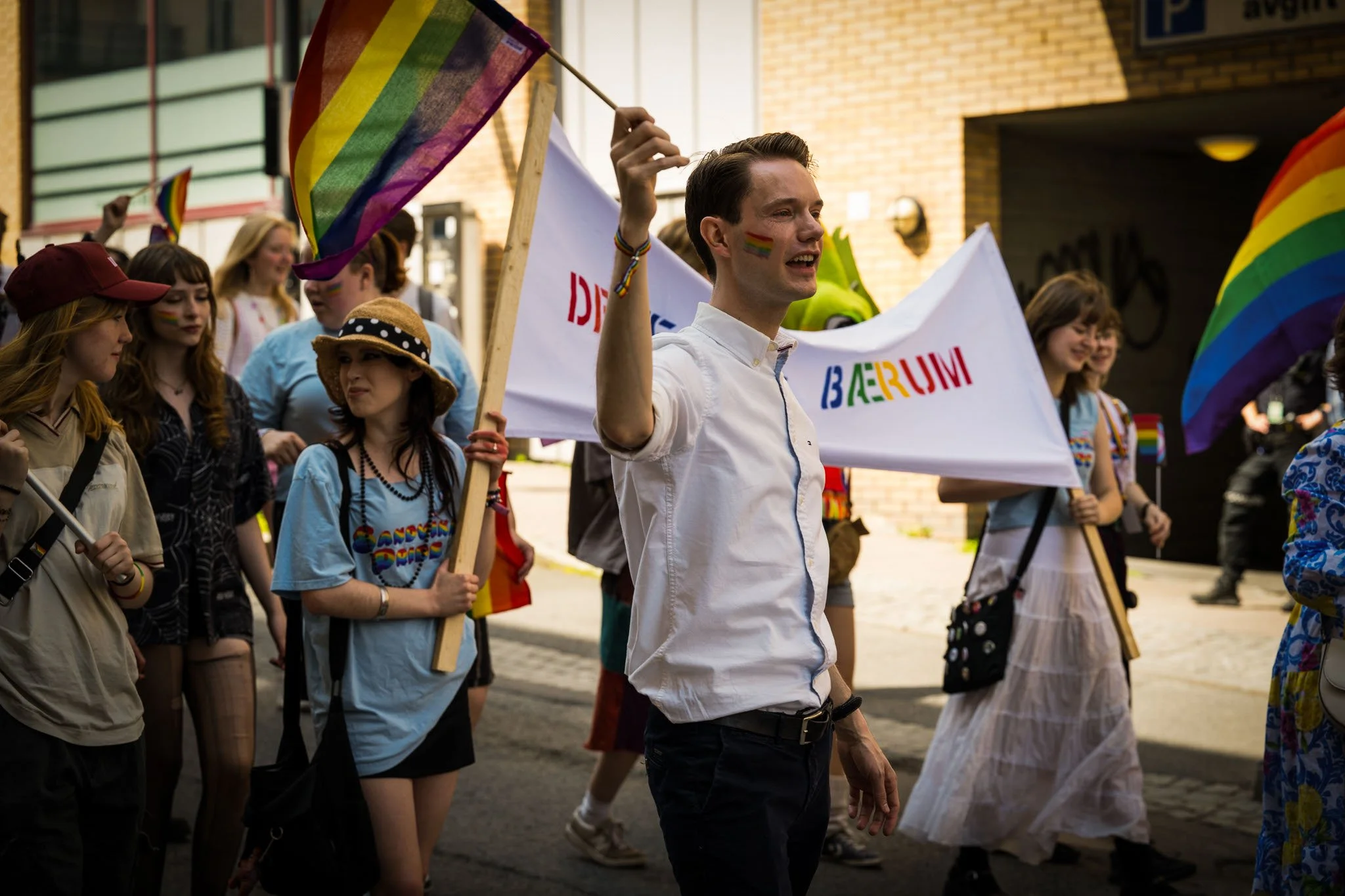 Personer deltar i en parademarsj med regnbueflagg, firer Pride med fartøy og fargerike klær, mange med regnbue- og stripsay-merkede elementer.