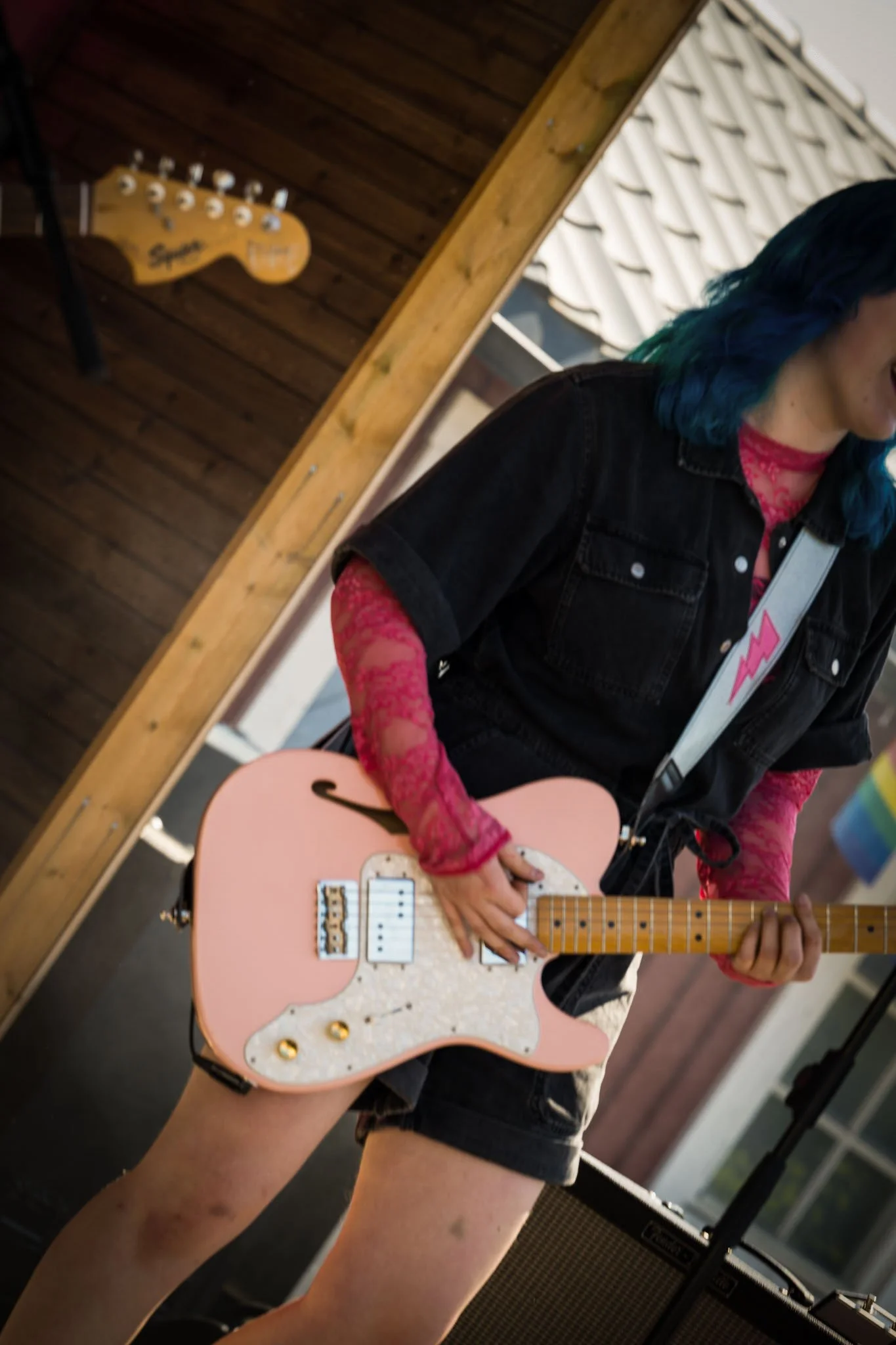 Person med blått hår spiller på en rosa elektrisk gitar.