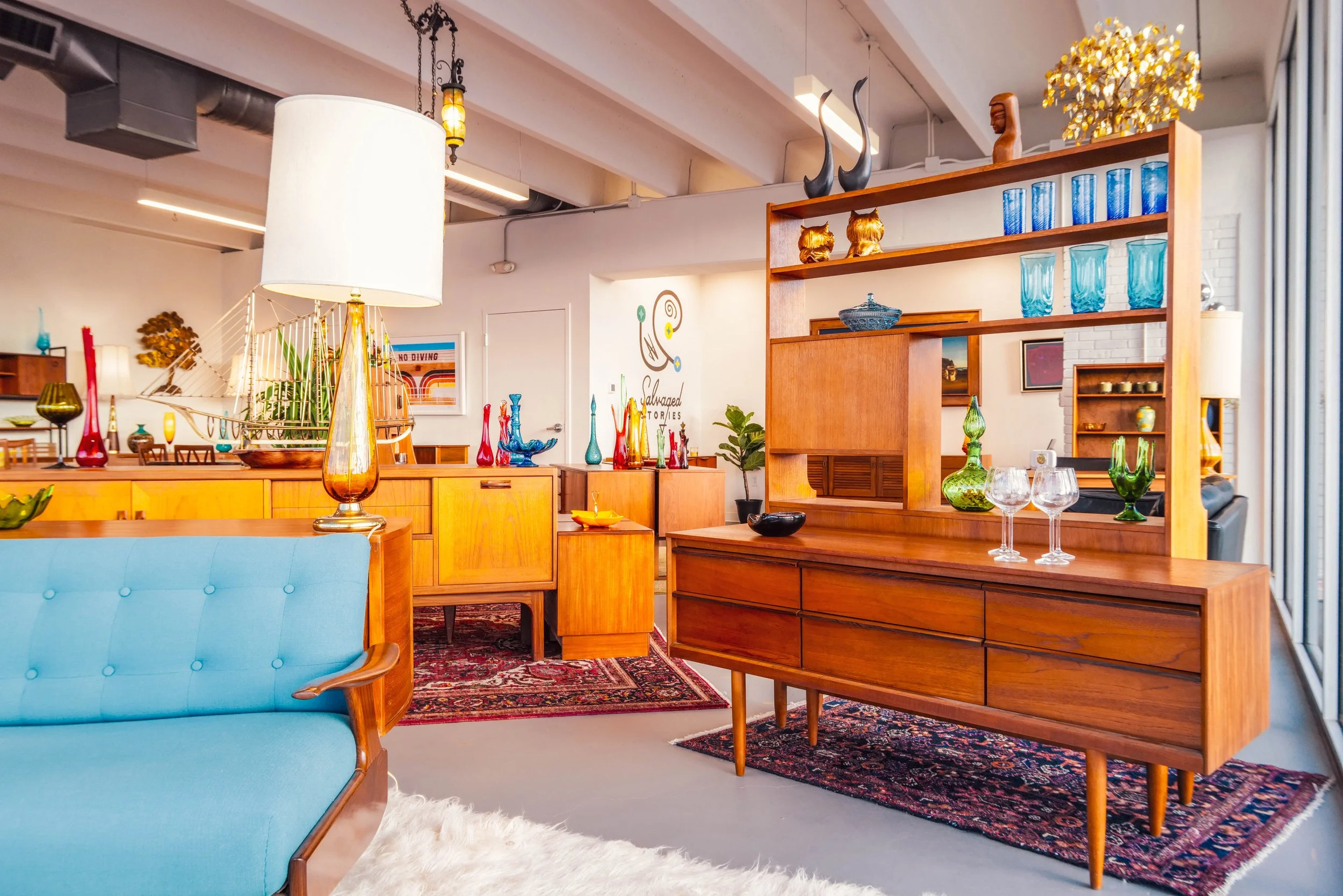 Interior of a modern living space with mid-century furniture, glass vases, artwork, and a patterned rug.