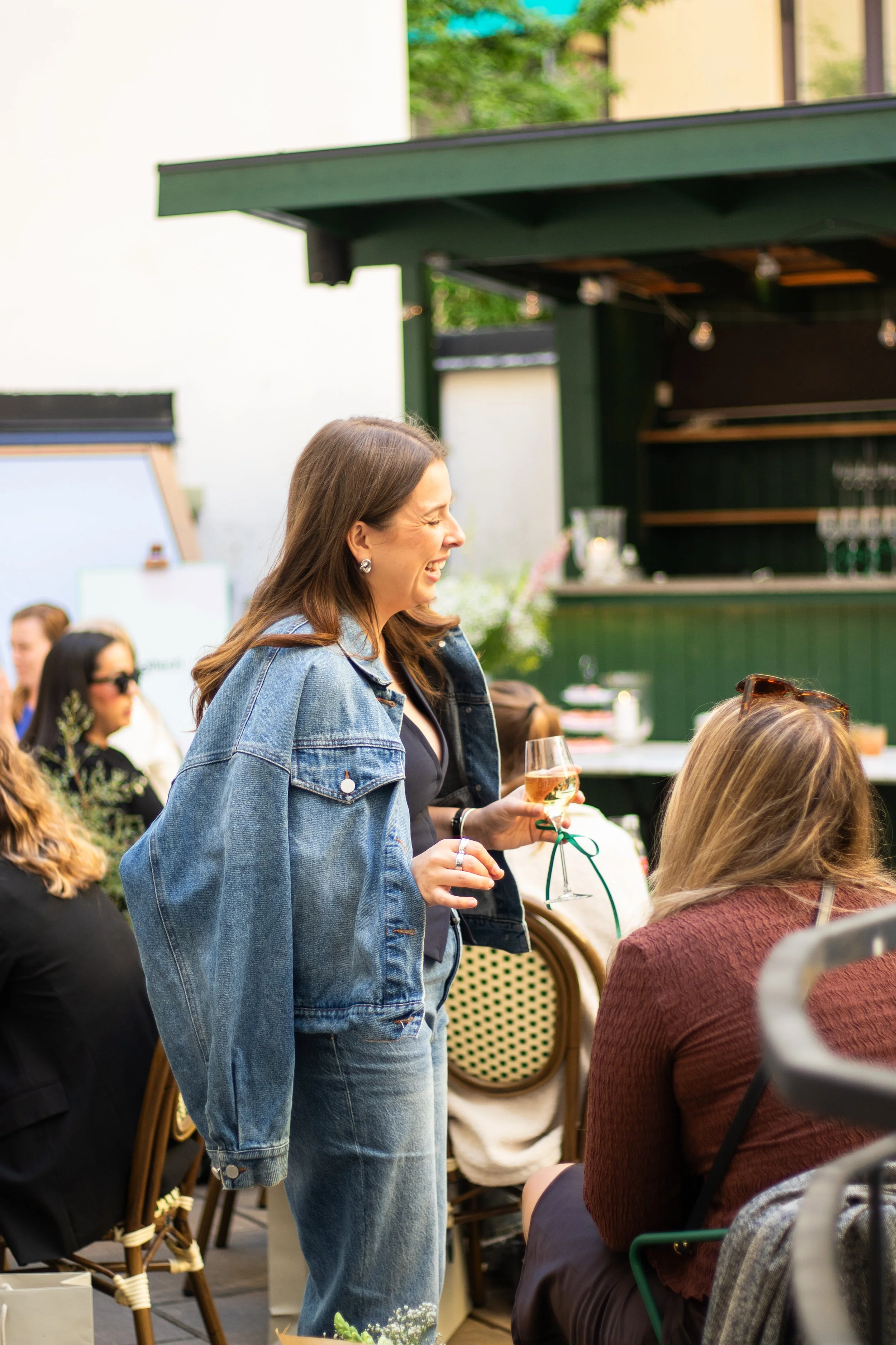 Event photography in Stockholm. Outside venue, sunny after-work event for a tech-company. Swedish influencer hosting with branded drinks and goodie-bags for guests. Guests sitting together at tables having conversation.