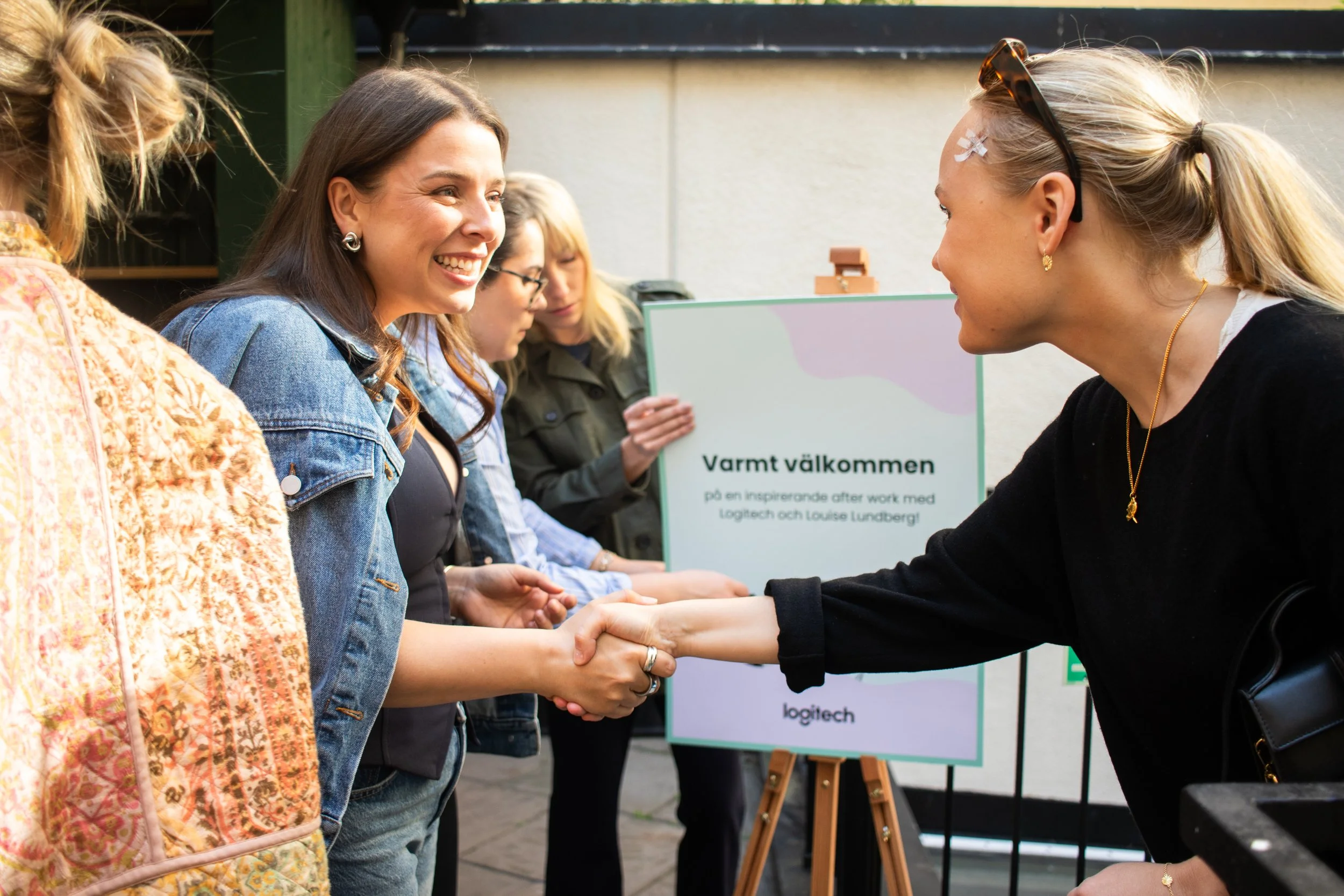 Event photography in Stockholm. Outside venue, sunny after-work event for a tech-company. Swedish influencer hosting with branded drinks and goodie-bags for guests. Hosts welcoming guests to the event. 