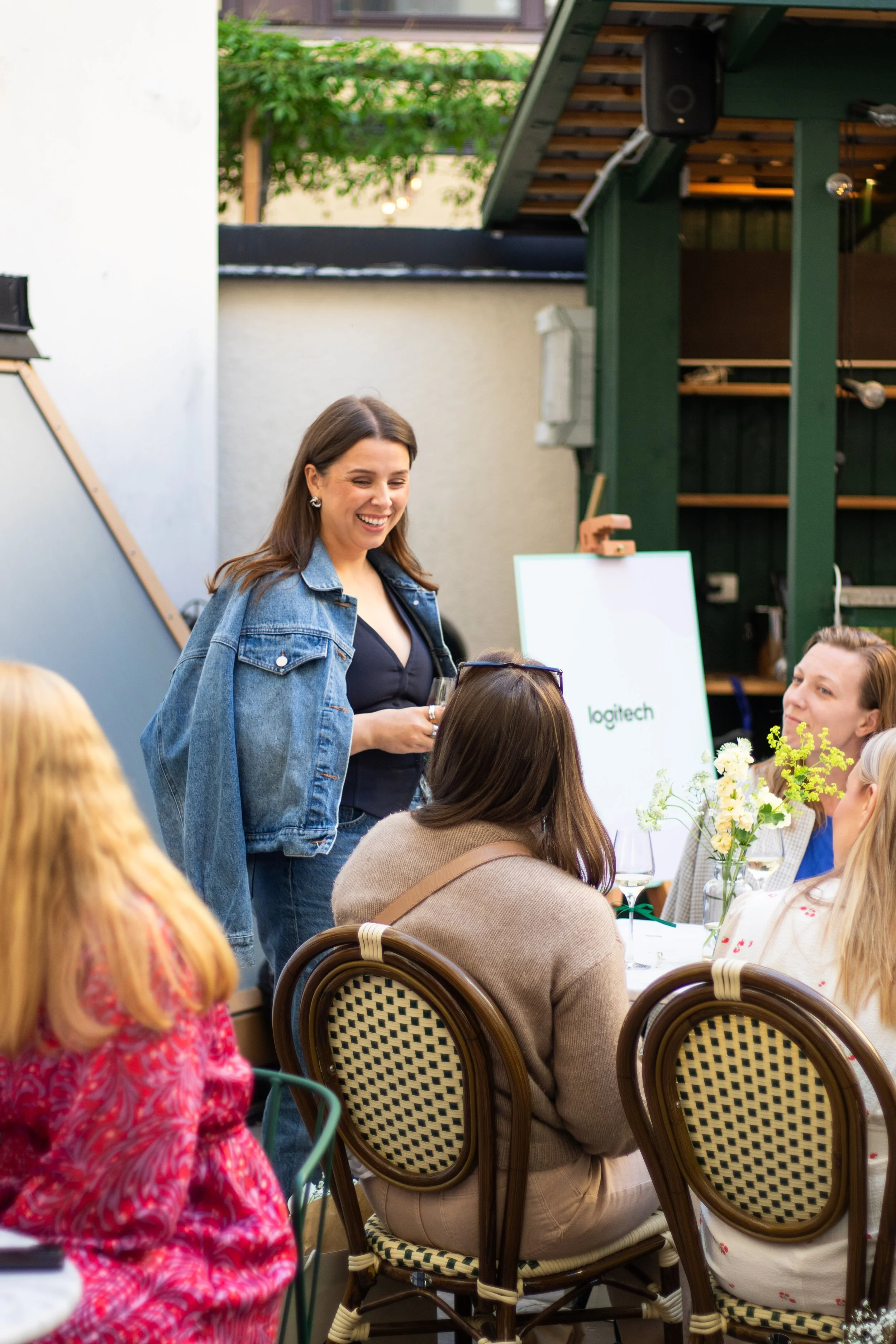 Event photography in Stockholm. Outside venue, sunny after-work event for a tech-company. Swedish influencer hosting with branded drinks and goodie-bags for guests. Guests sitting together at tables having conversation.