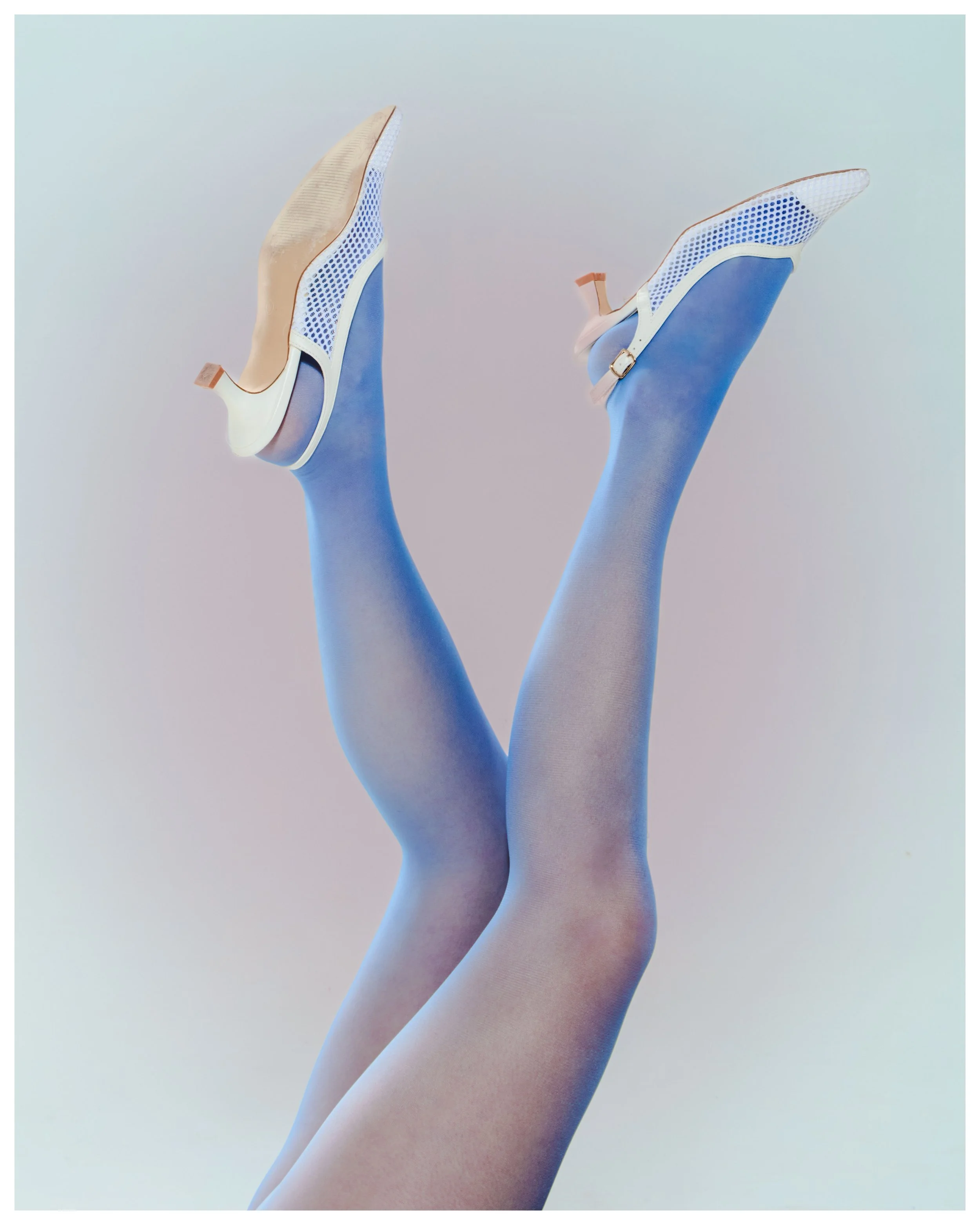 Legs in blue tights wearing white heels with blue accents, raised in the air against a plain background.