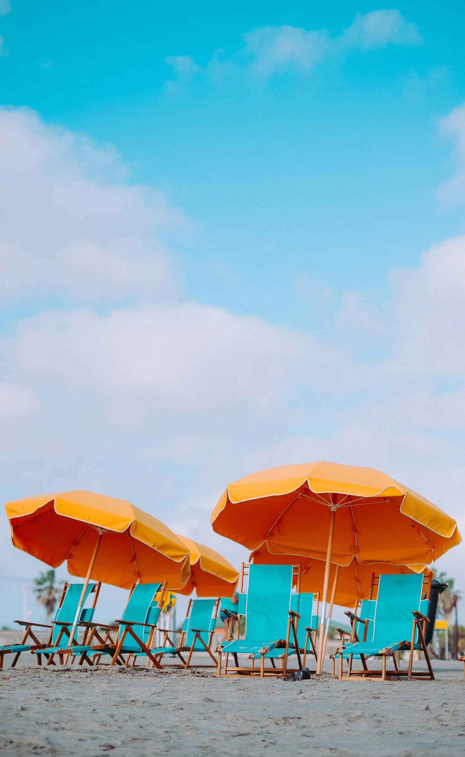 Empty beach chairs with orange umbrellas on sandy beach under cloudy sky.