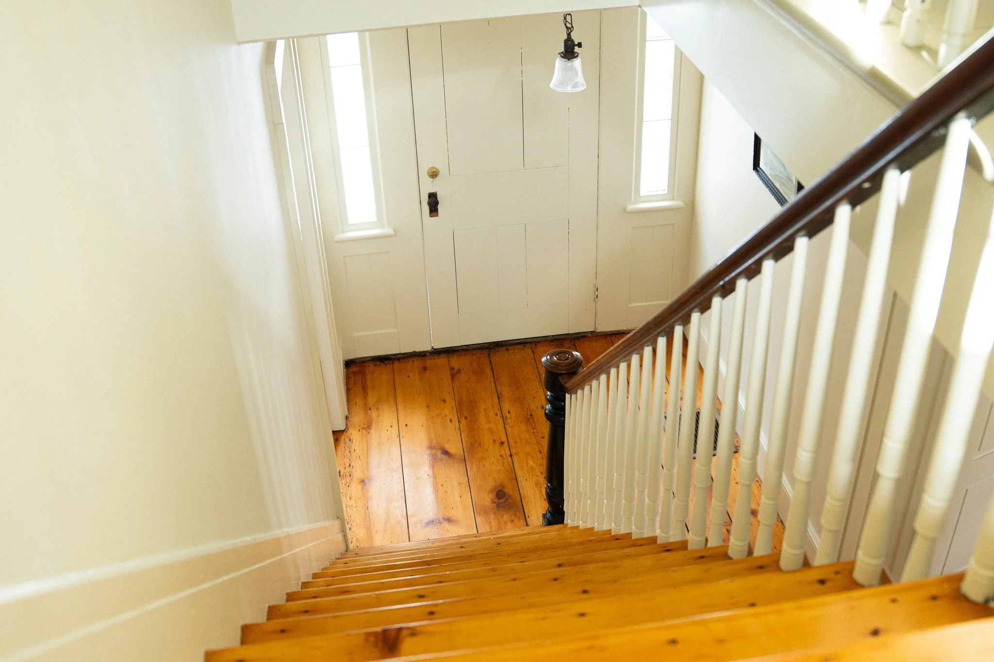 Wooden staircase leading down to a white front door with two small windows outside.
