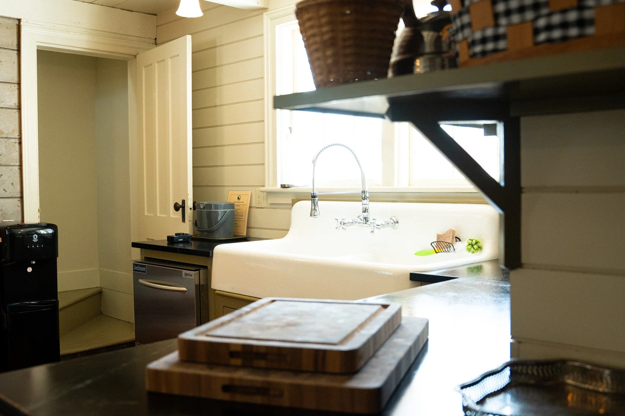 Kitchen with farmhouse sink, window, cutting boards, and black checkered jars on a shelf.