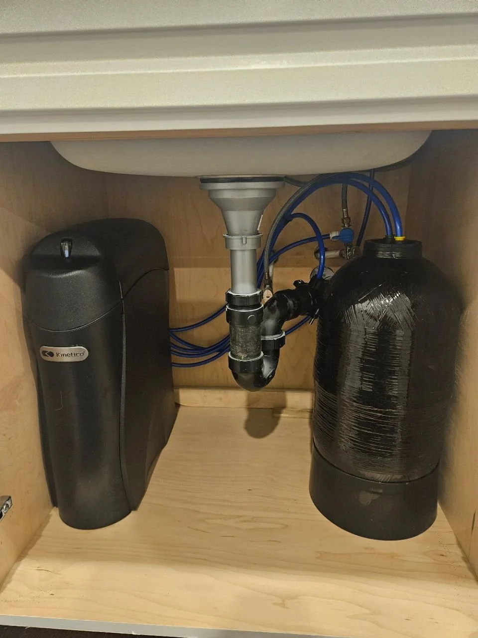 An image of a Kinetico K5 Reverse Osmosis Drinking Water System attached to a black water storage tank underneath a sink.