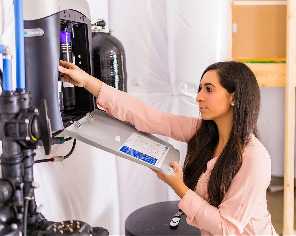 An image of a woman changing the filter cartridges inside a Kinetico K5 Reverse Osmosis Drinking Water System.